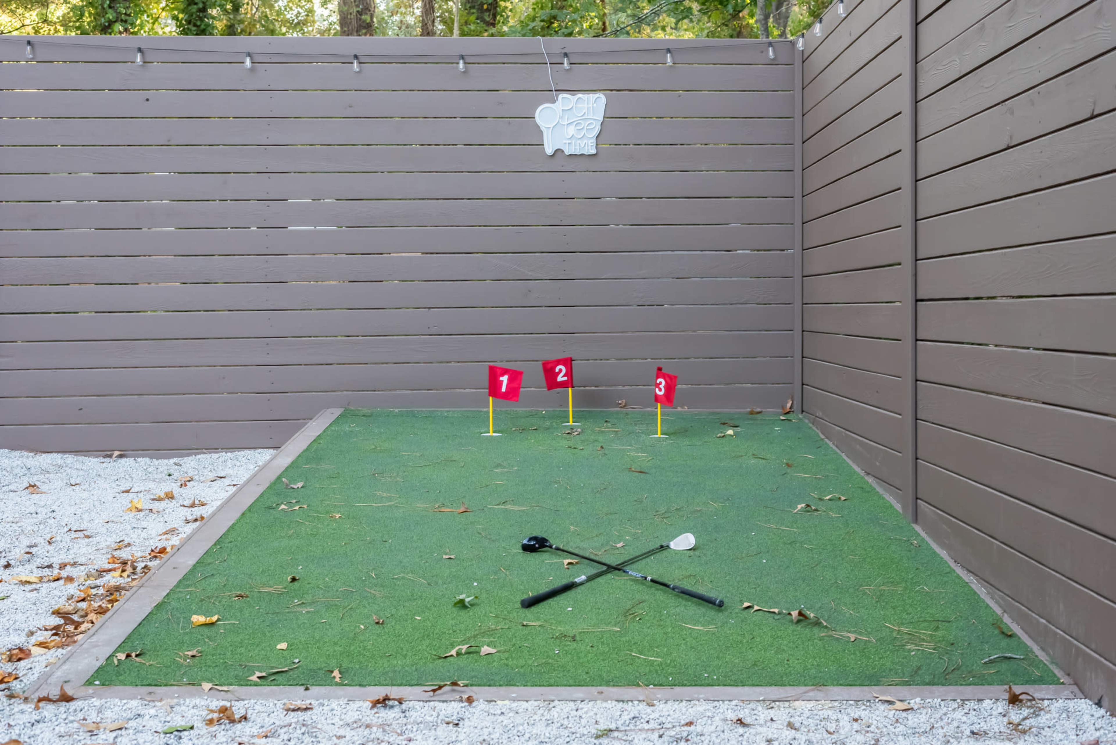 The image shows a small putting area with three flags numbered one to three on artificial grass, surrounded by a wooden fence.