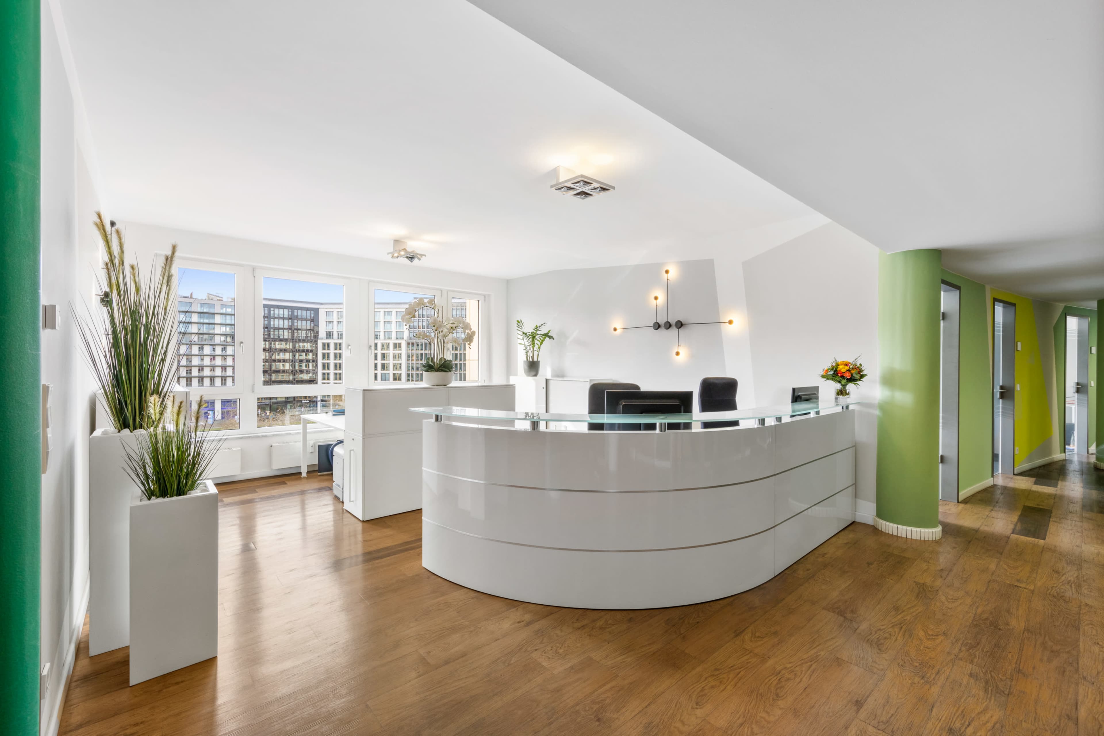A modern reception area features a curved desk, wooden flooring, and large windows overlooking a cityscape.