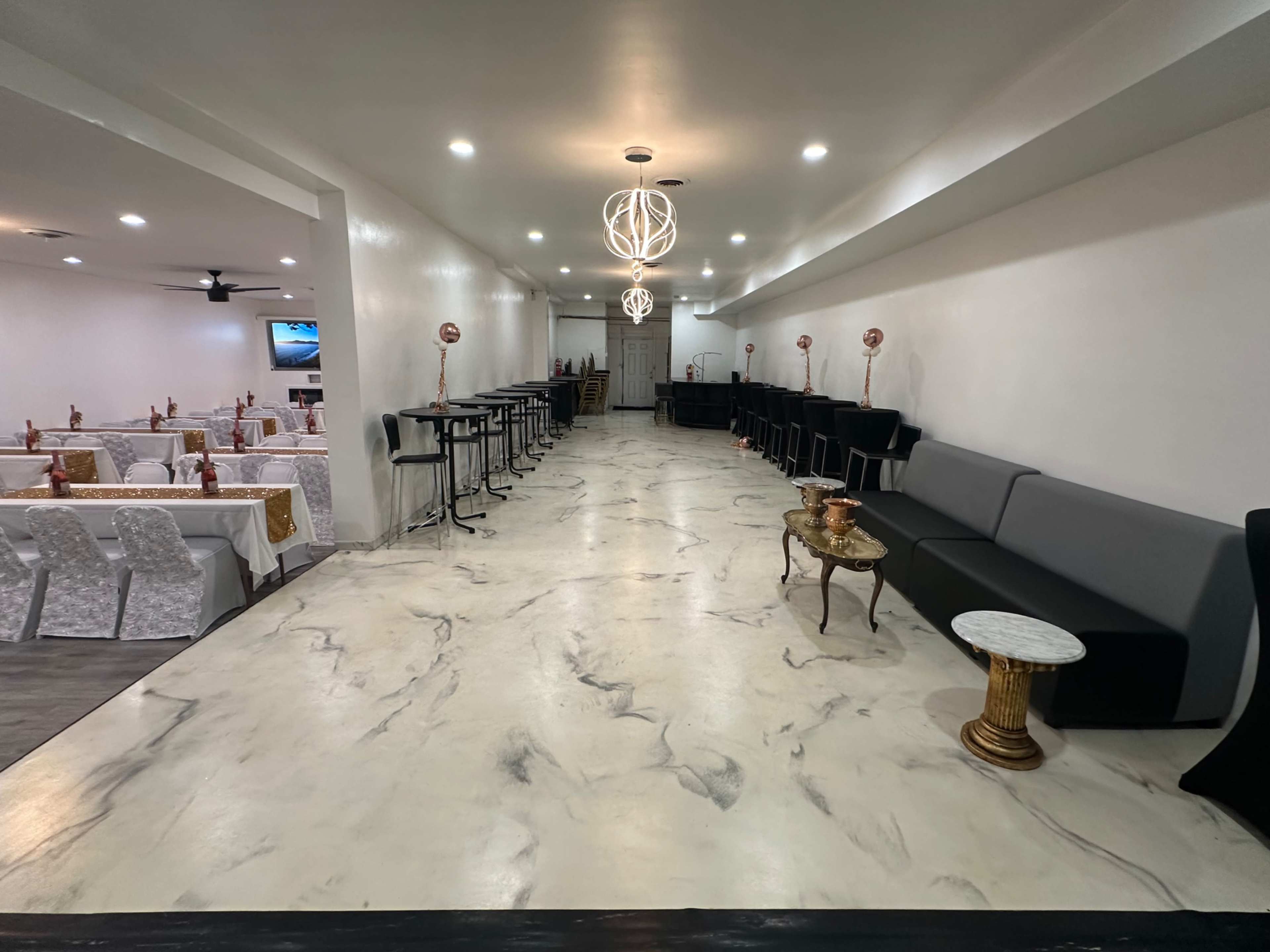 The image shows a spacious restaurant interior with a long, marble-patterned floor, seating areas along the sides, and decorative lighting fixtures overhead.