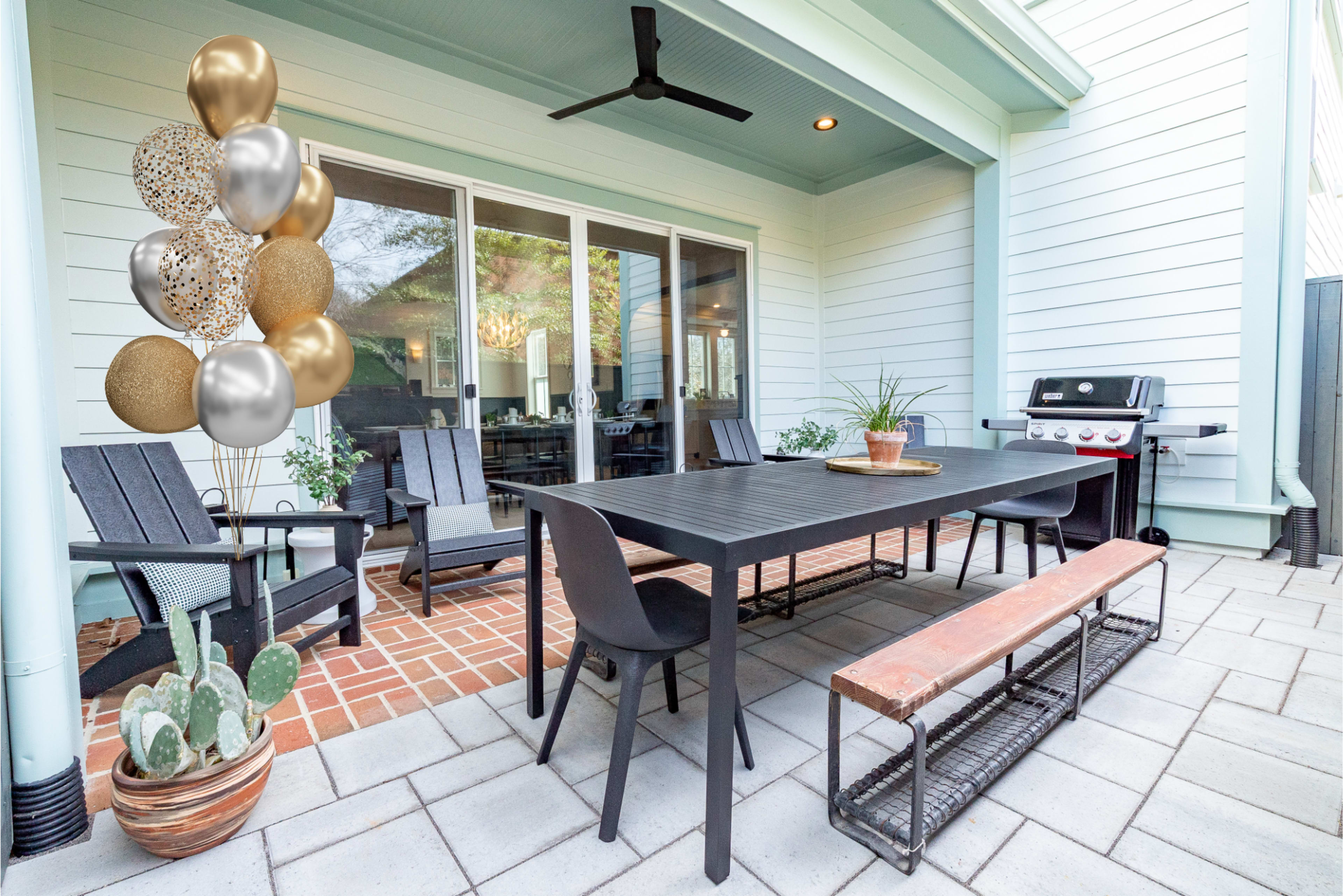 The image shows a patio area with a large table, several chairs, a grill, potted plants, and decorative balloons on one side.