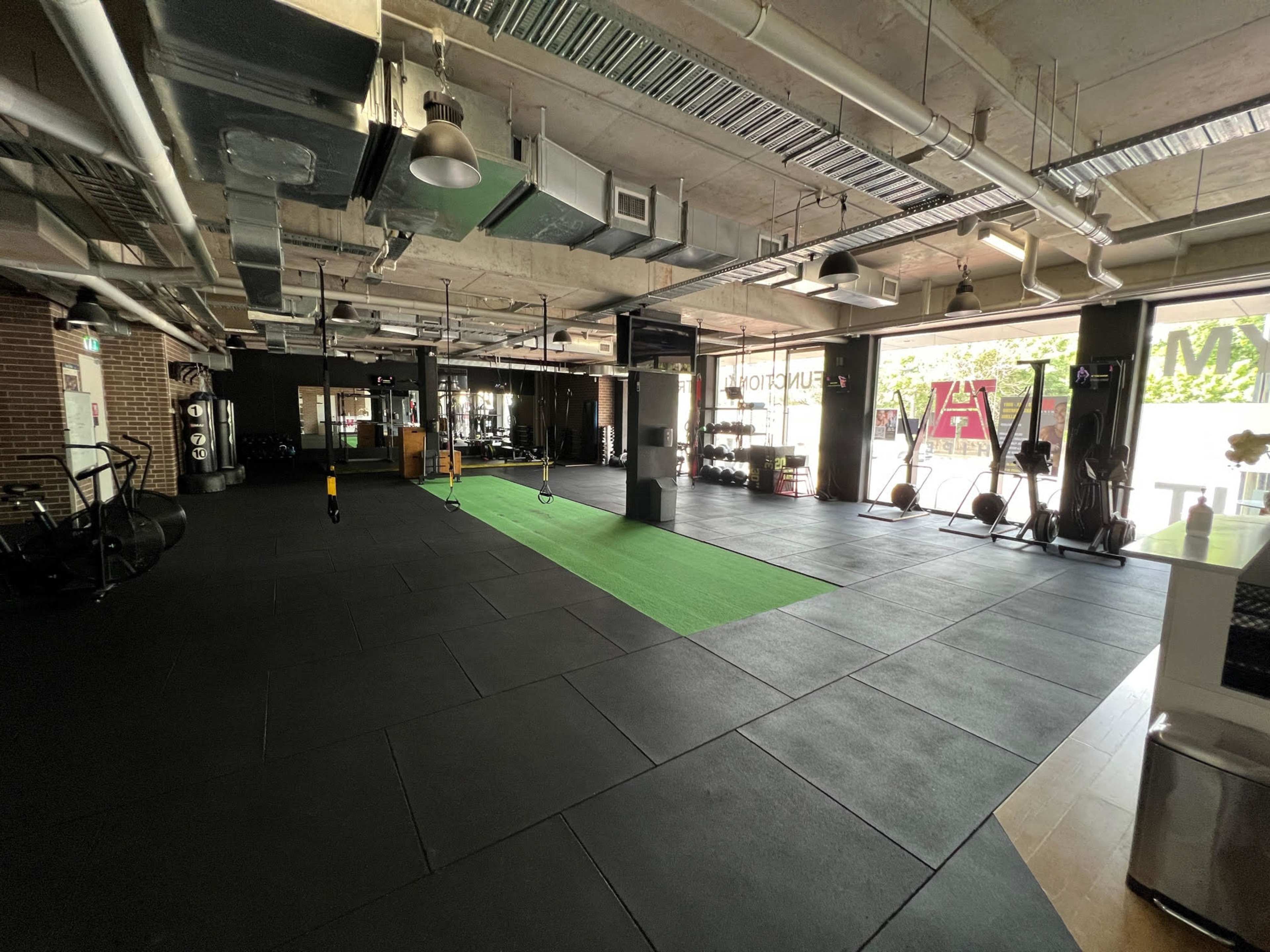 A spacious gym interior with black flooring, green turf in the center, and various exercise equipment along the walls.