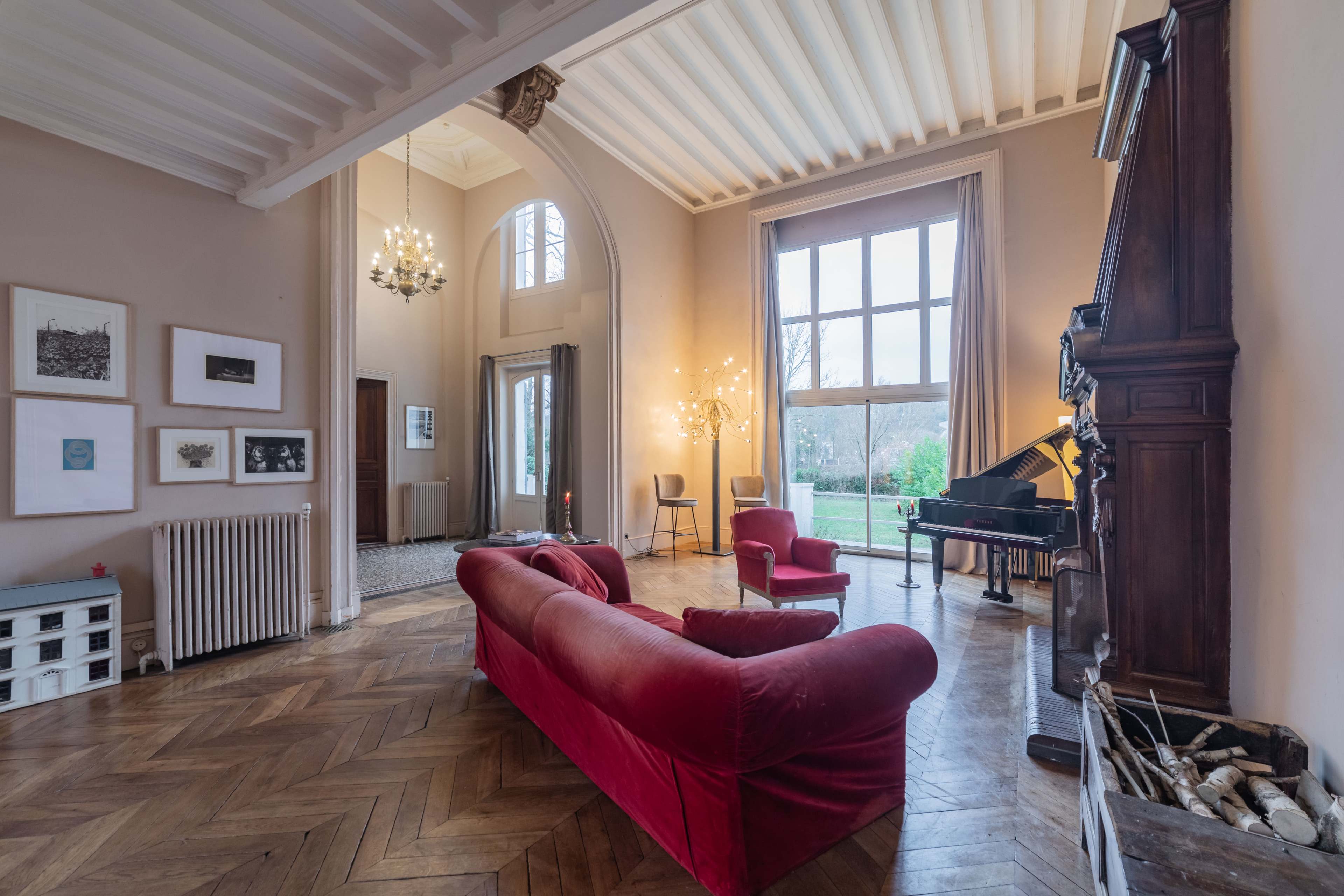 A spacious living room with a red velvet sofa, a grand piano, and large windows overlooking a garden.