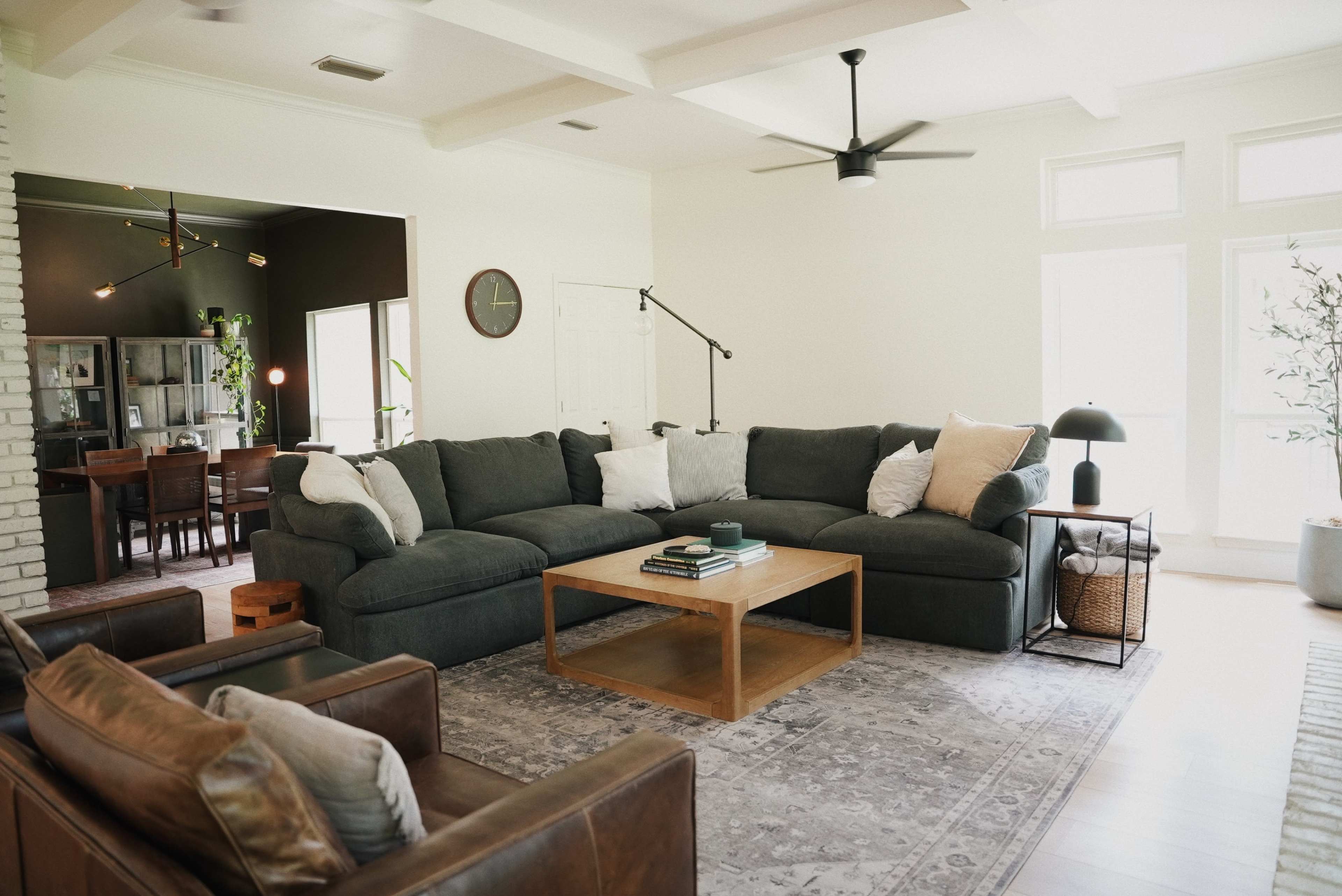 The living room features a large sectional sofa, a wooden coffee table, and an adjacent dining area with a dark wall.