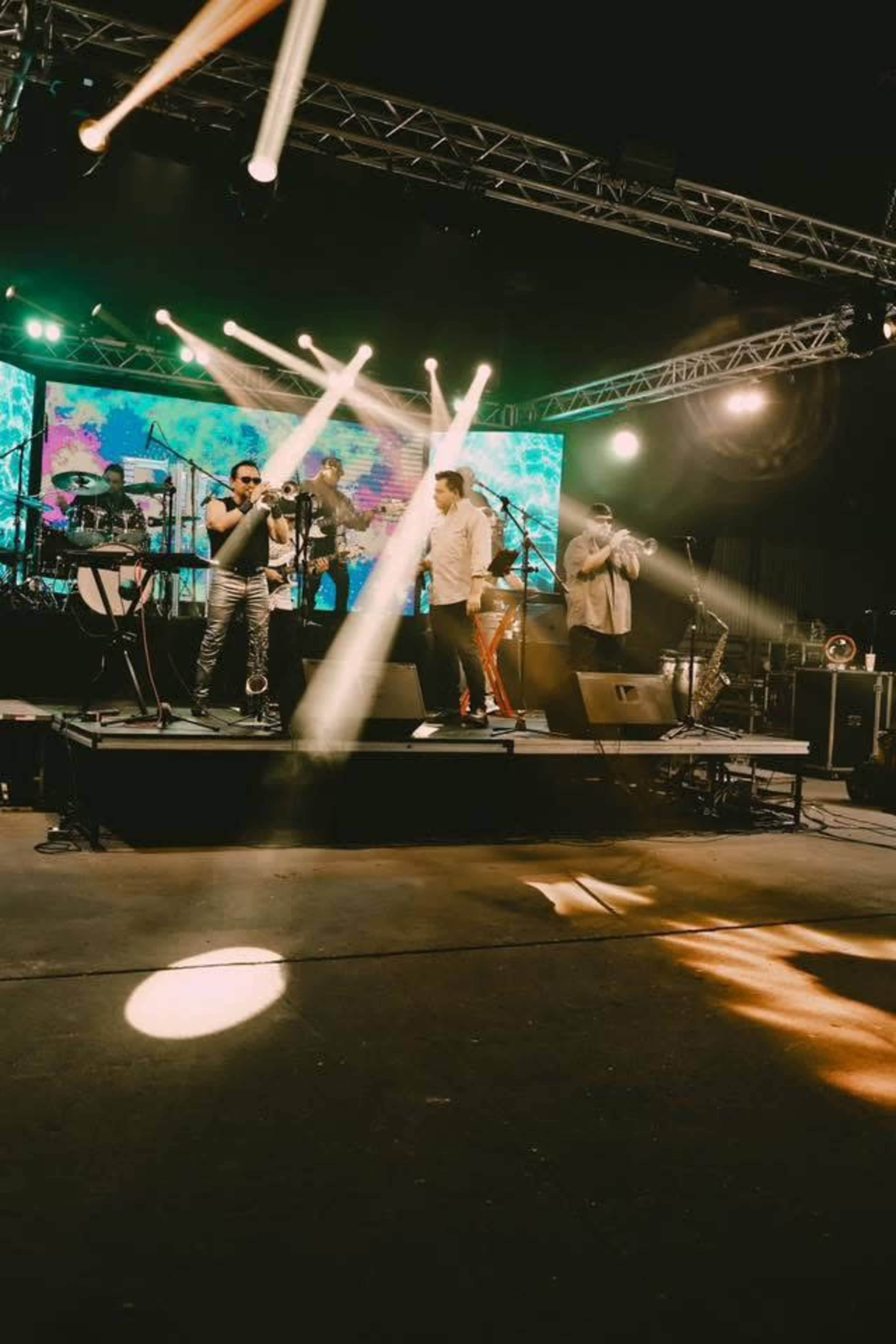 A band performs on stage under bright lights with various instruments arranged around them.