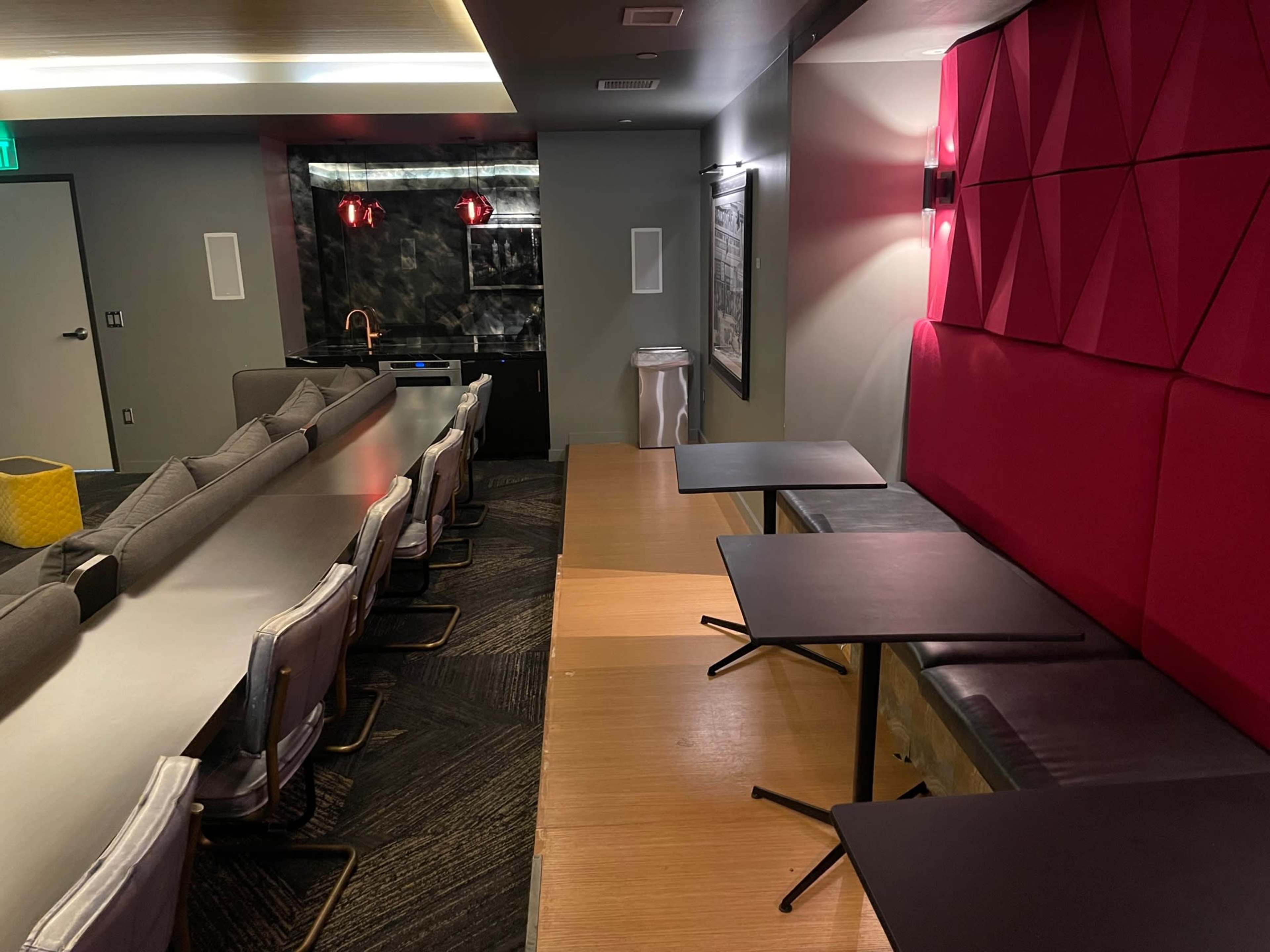 A modern lounge area featuring a combination of seating, tables, and a kitchenette against a wall.