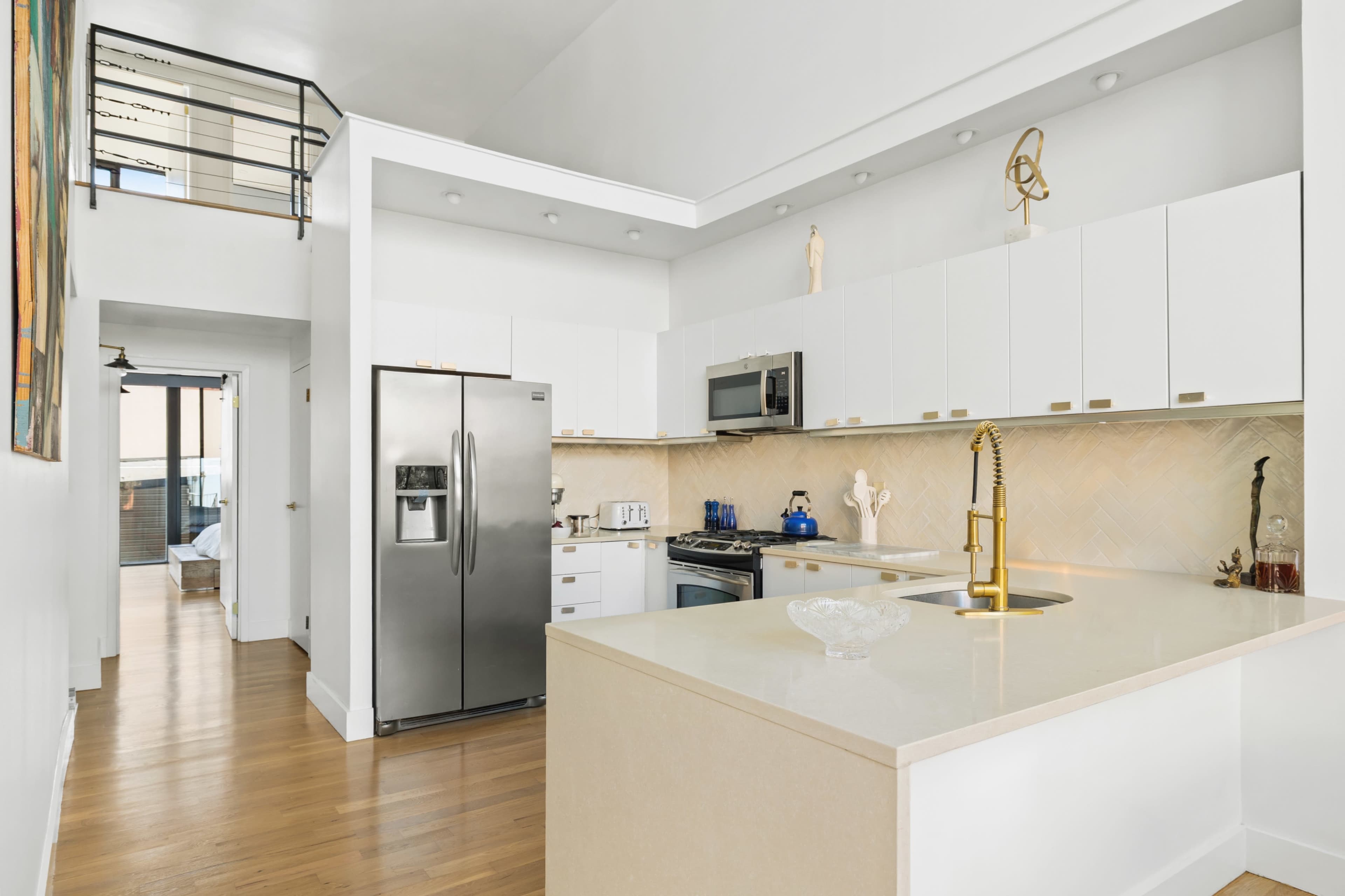 The image shows a modern kitchen with white cabinetry, a stainless steel refrigerator, and a central island with a sink.