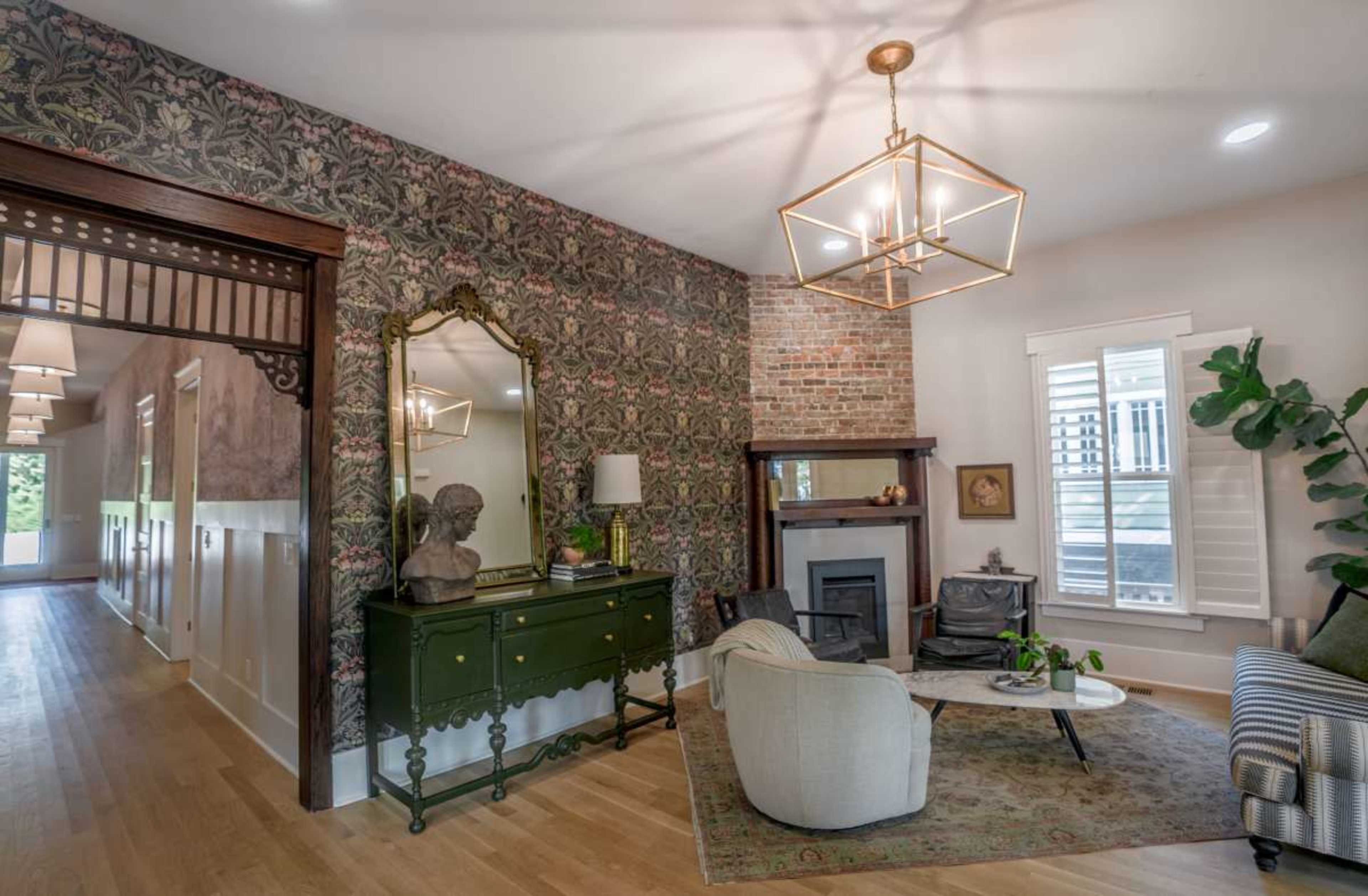 The image shows a living room with a mix of vintage and modern decor, featuring a green sideboard, a mirror, a seating area with a couch, and exposed brick walls.