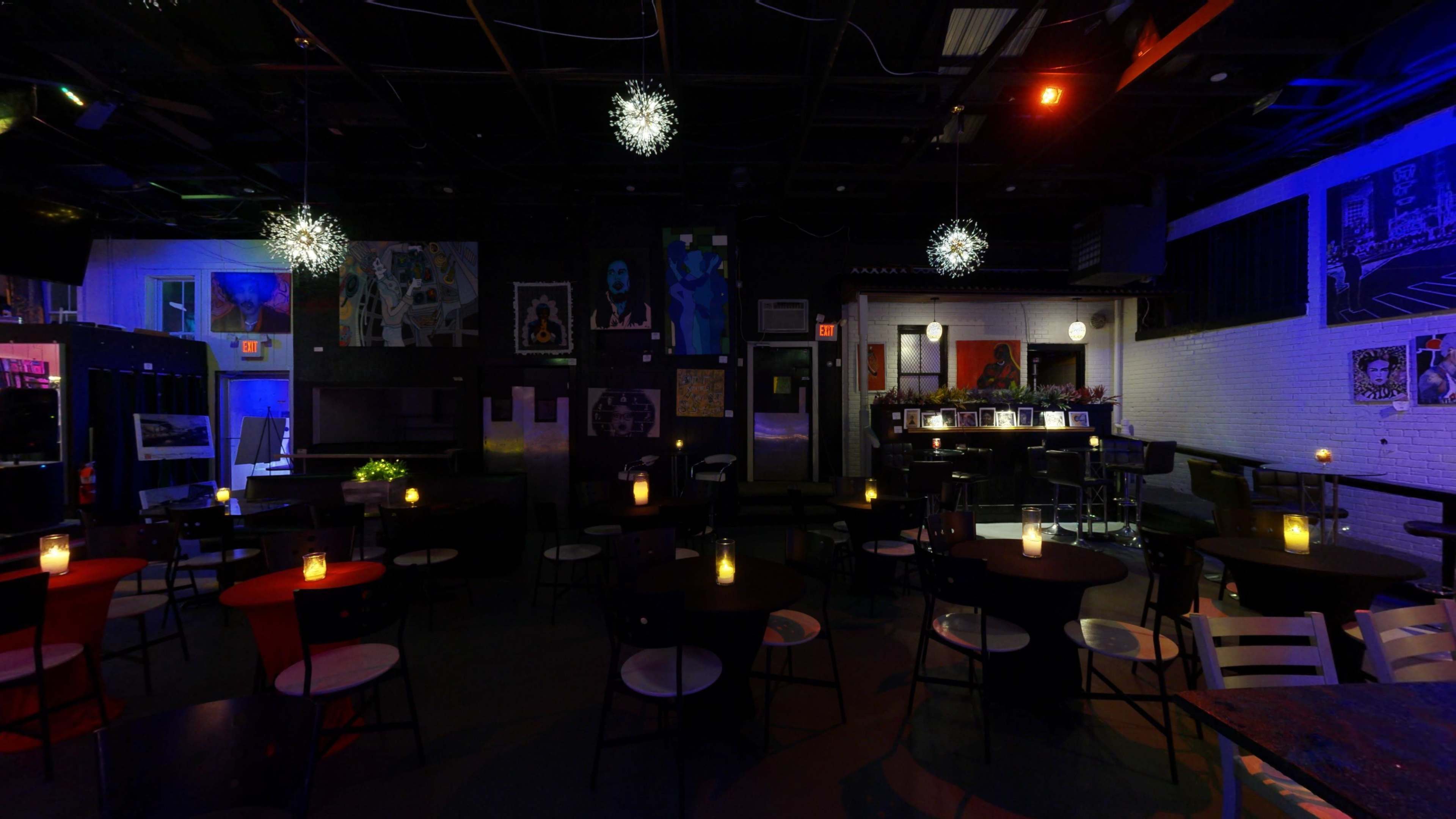 A dimly lit bar scene features circular tables surrounded by chairs, with hanging light fixtures and artwork on the walls.