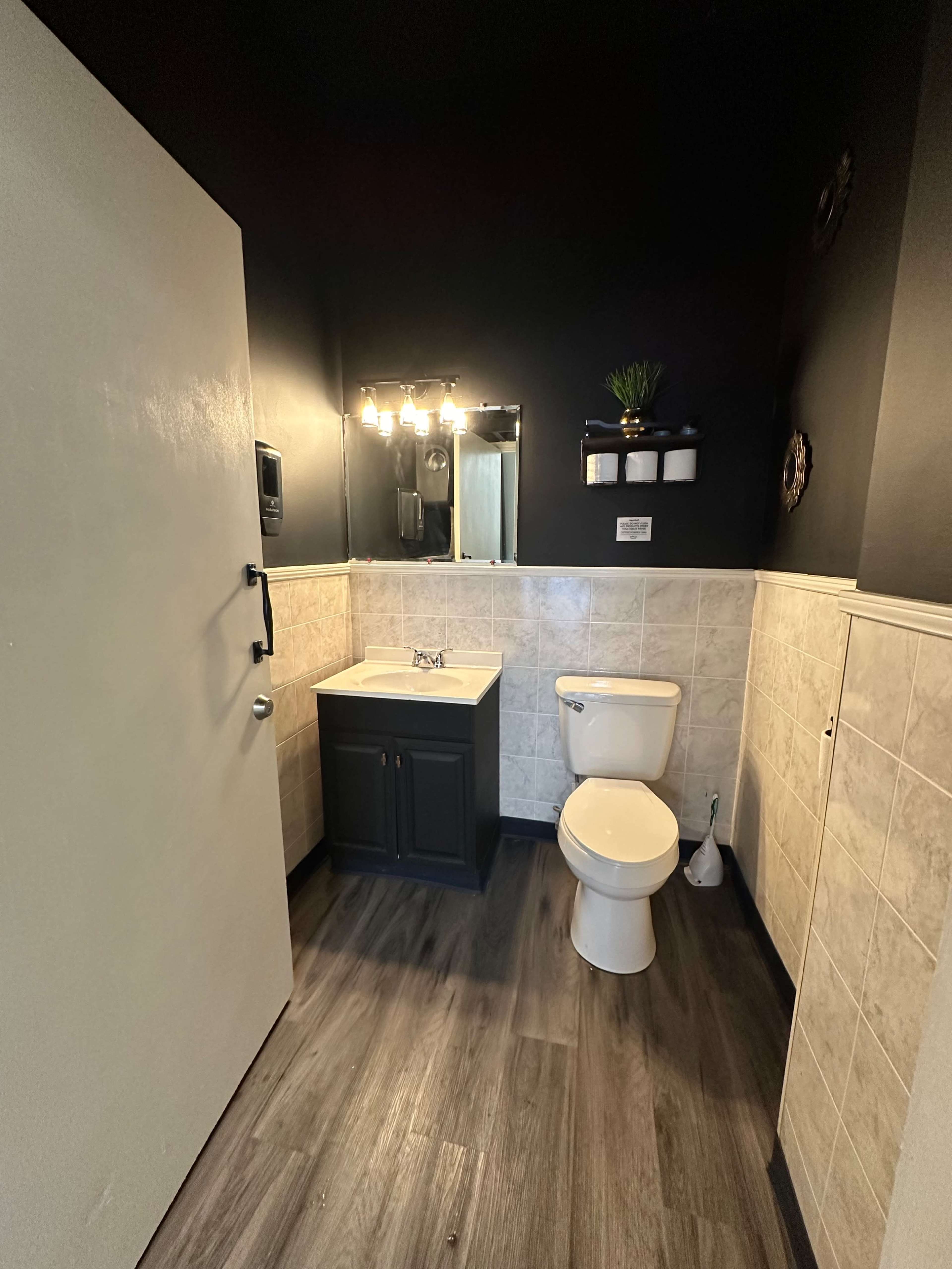 A small bathroom featuring a toilet, a sink with a dark cabinet, a mirror, and a textured tiled wall.