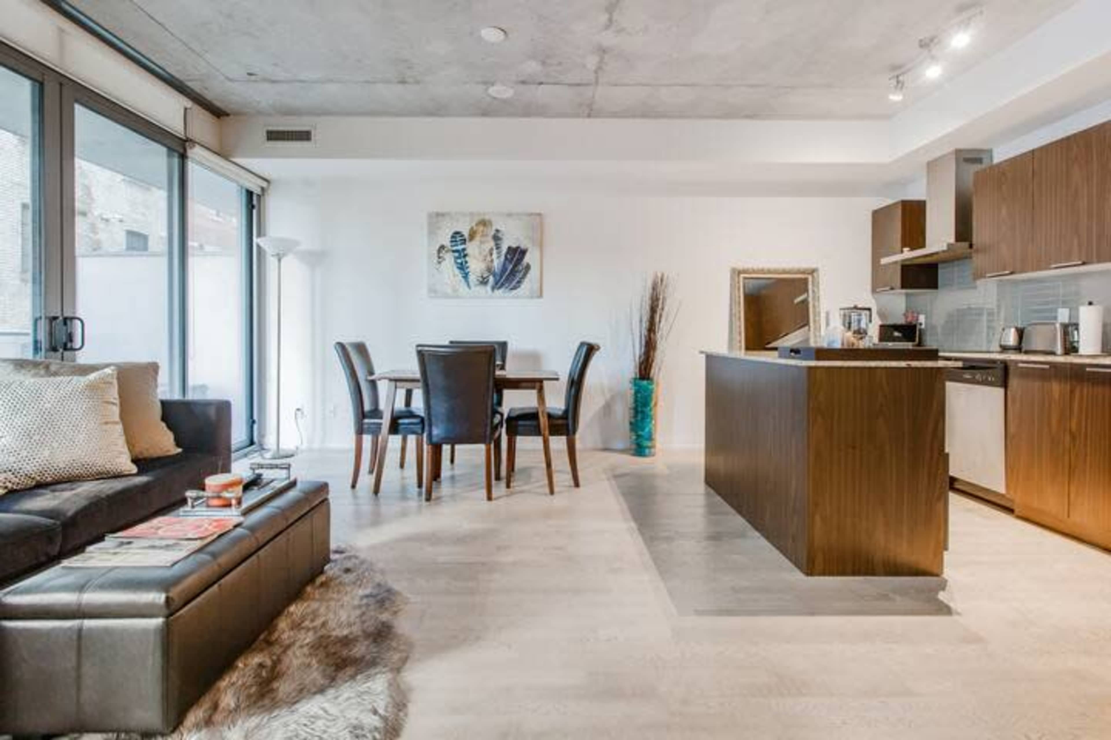 A modern, open-concept apartment featuring a kitchen, dining area with a table, and a living room with a sofa and decor items.