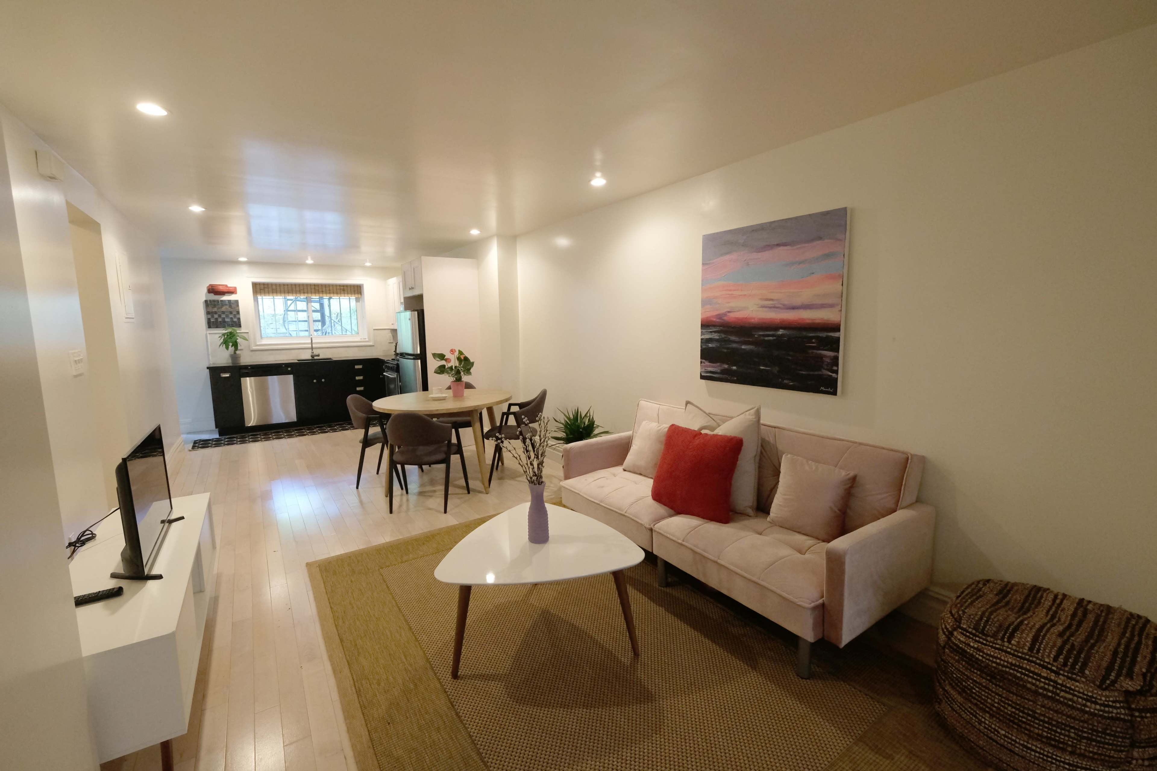 A modern living space features a light-colored sofa, a round dining table, and a kitchen visible in the background.