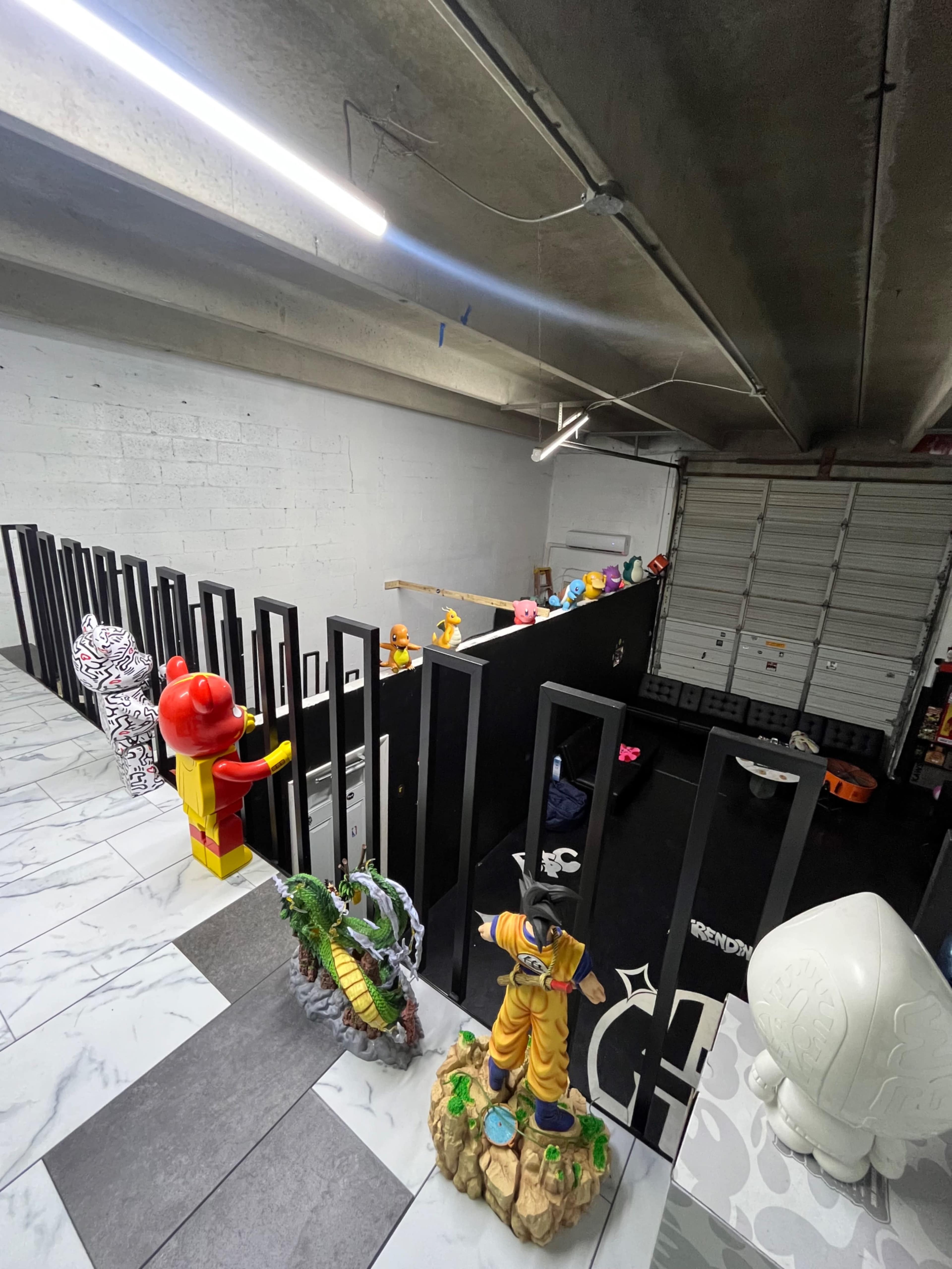 The image shows a garage-like space with a black wall featuring colorful figurines lined up along a railing.
