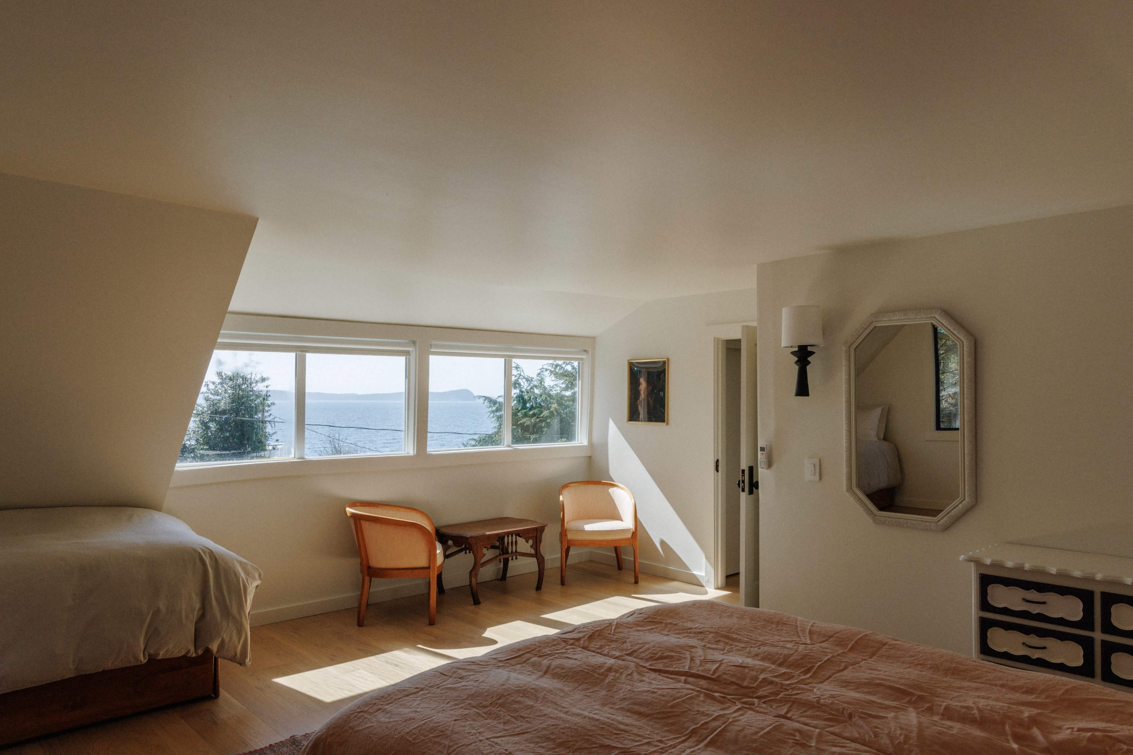 The room features two beds, a small table with chairs, and large windows overlooking a scenic view.