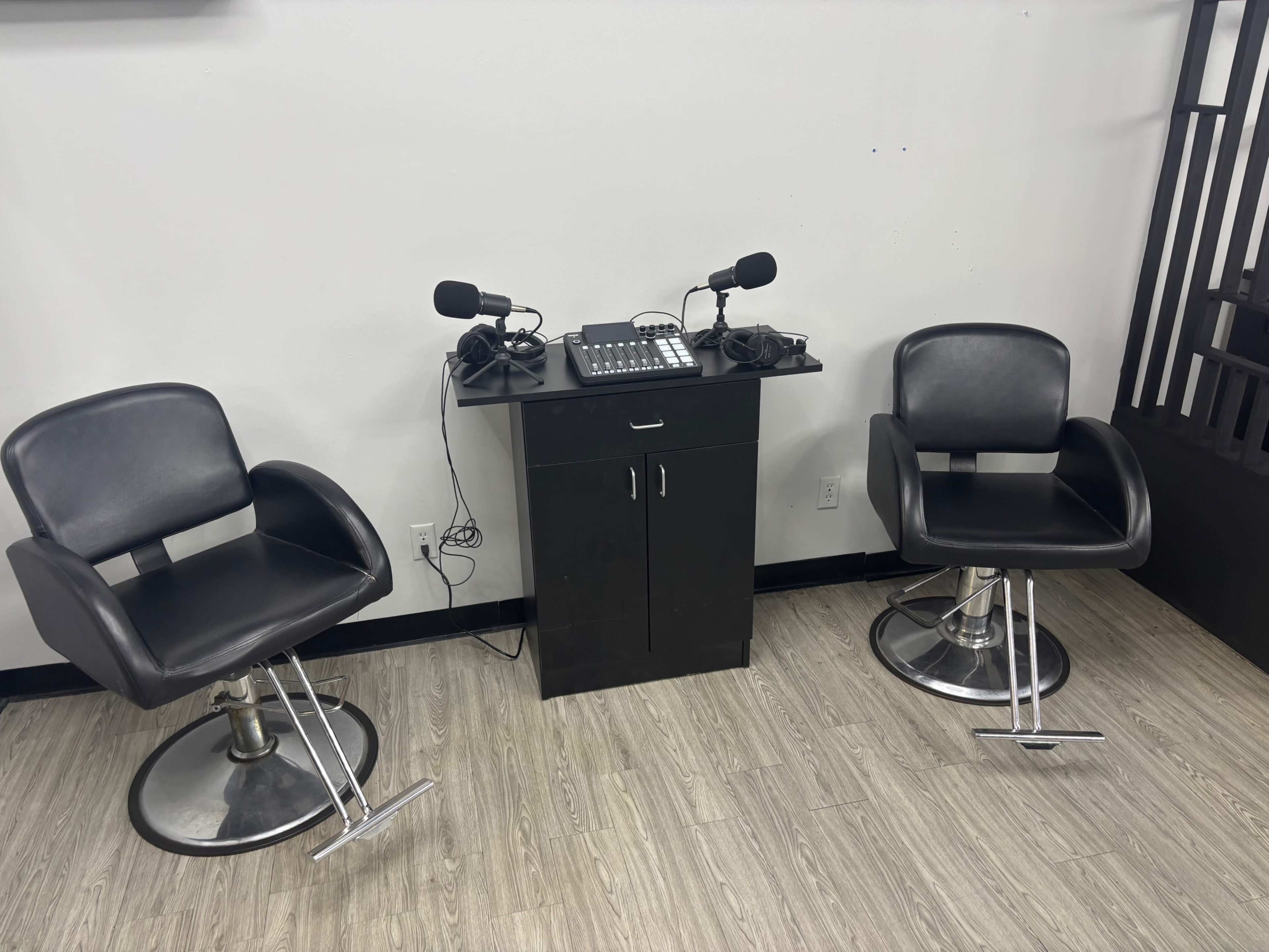 The image shows two black swivel chairs positioned in front of a small control panel with microphones and equipment on a table.