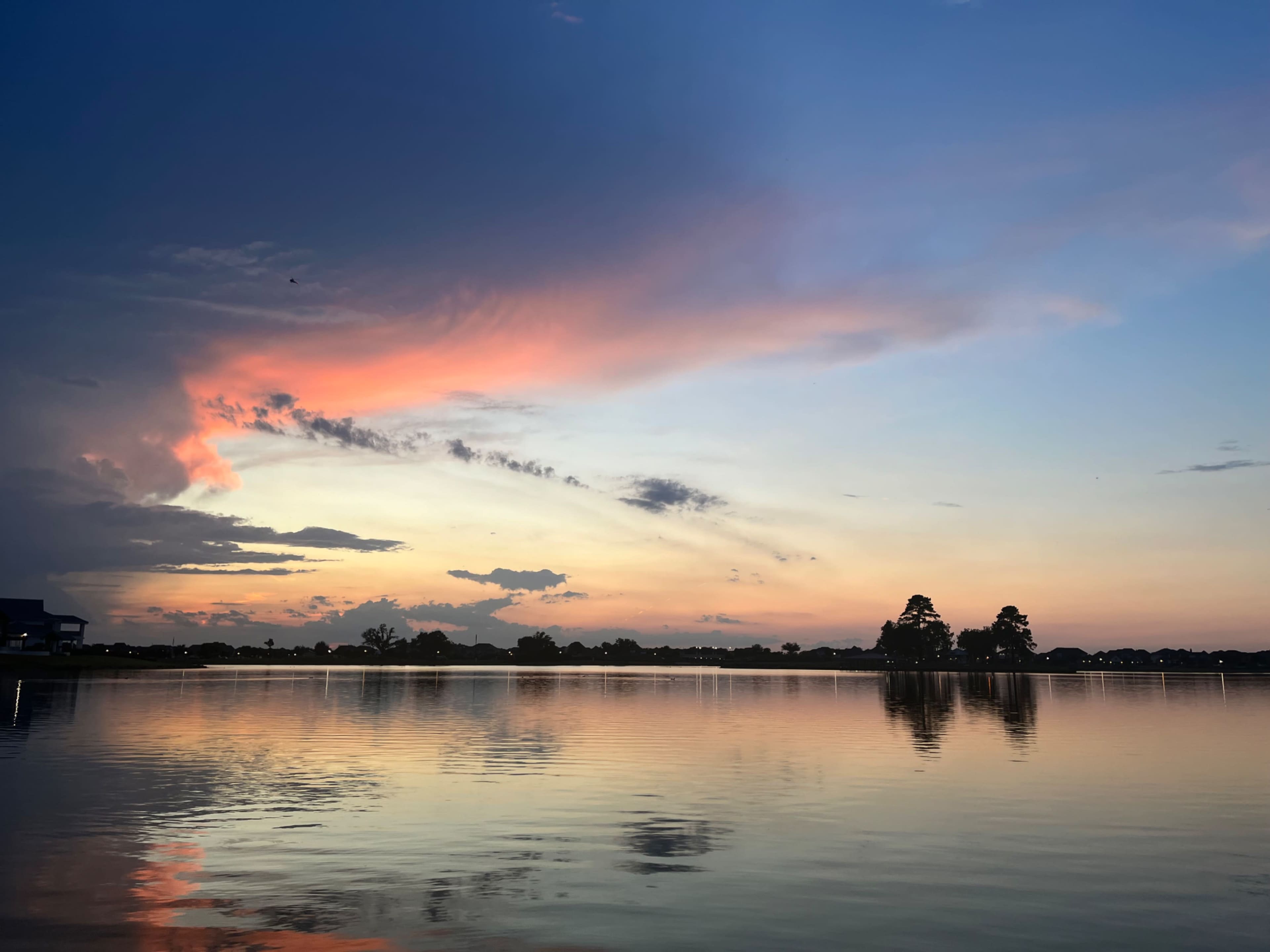 The scene shows a tranquil lake reflecting a colorful sunset with clouds against a clear sky.