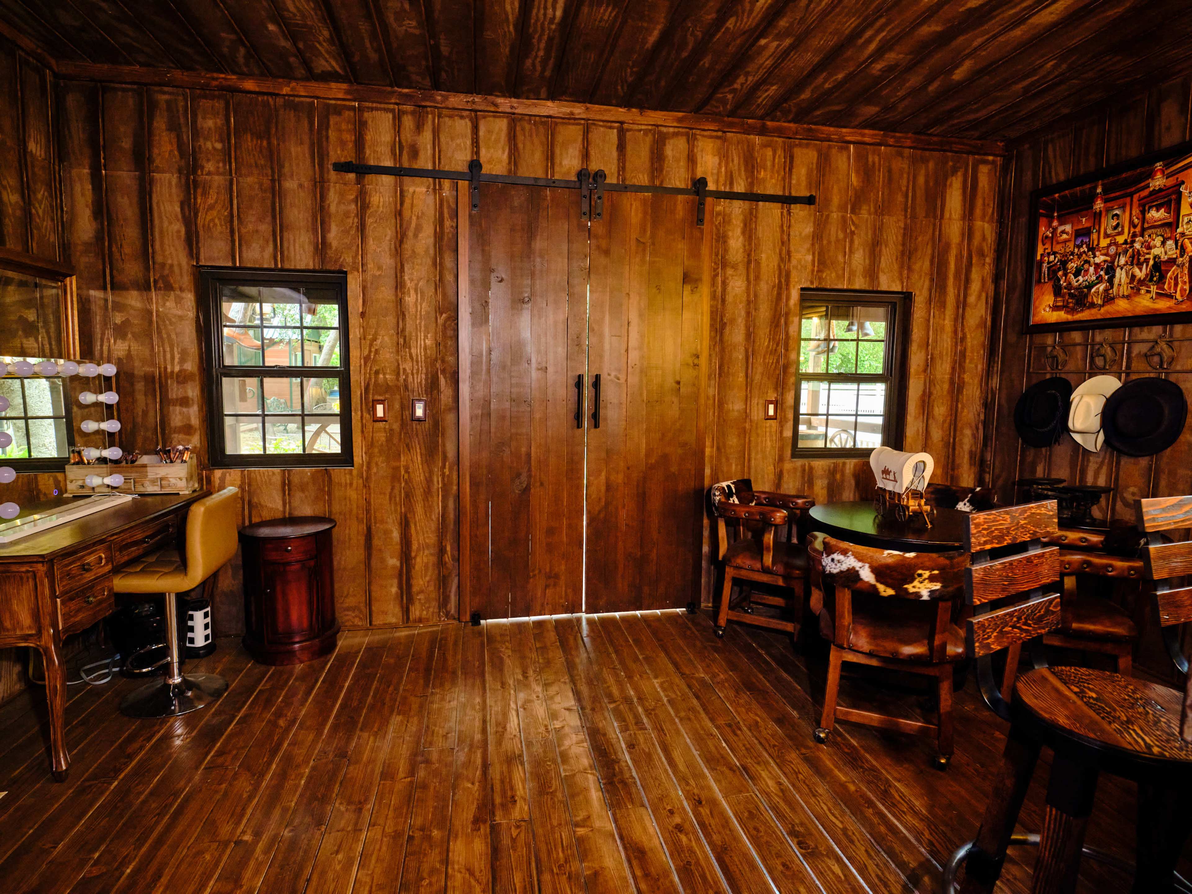 A rustic wooden interior with two large sliding doors, a vanity table, and various wooden furniture pieces arranged around a circular table.