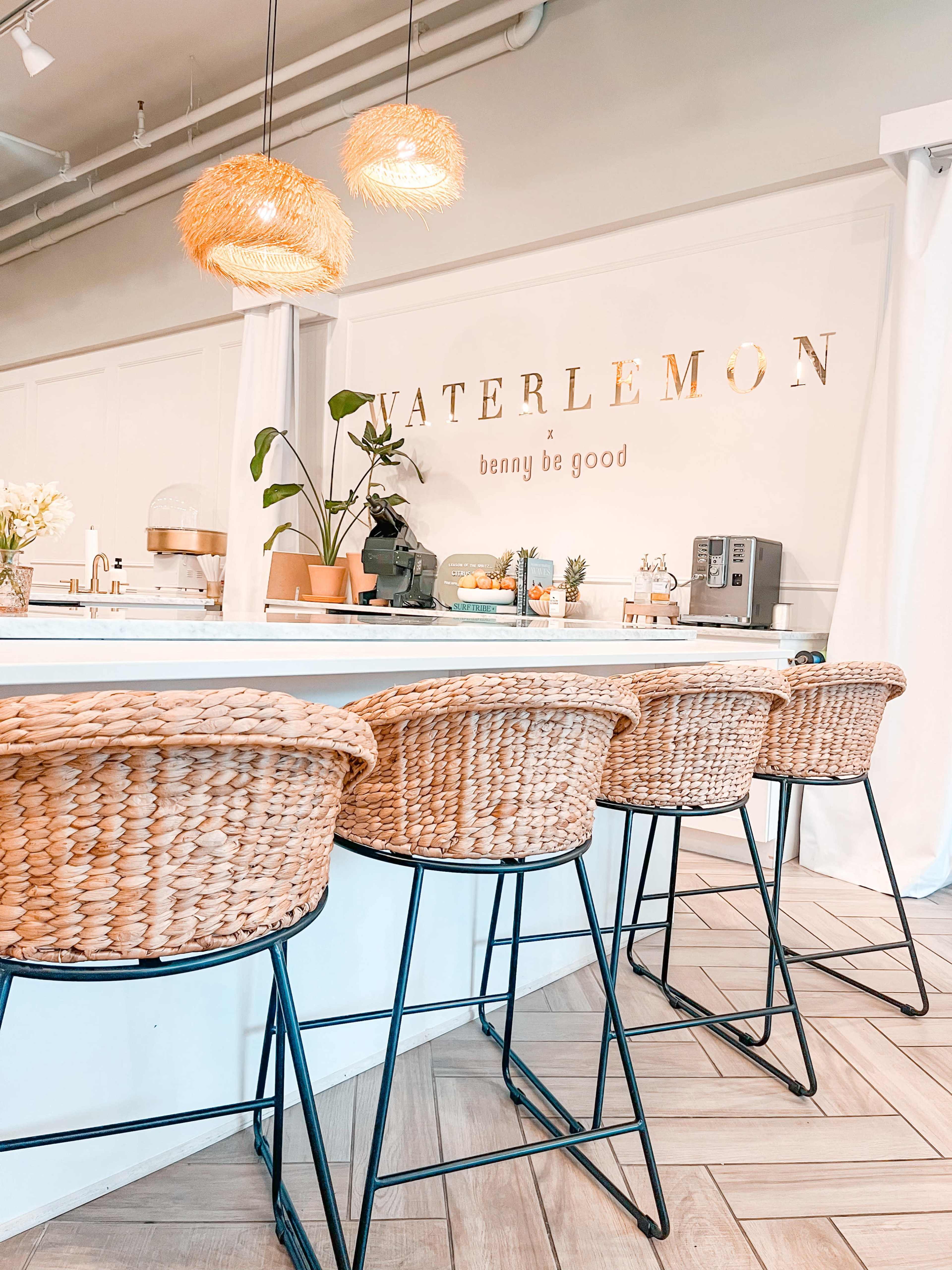 The image shows a modern café interior featuring a white counter, woven bar stools, and decorative lighting, with the word "WATERLEMON" displayed on the wall.