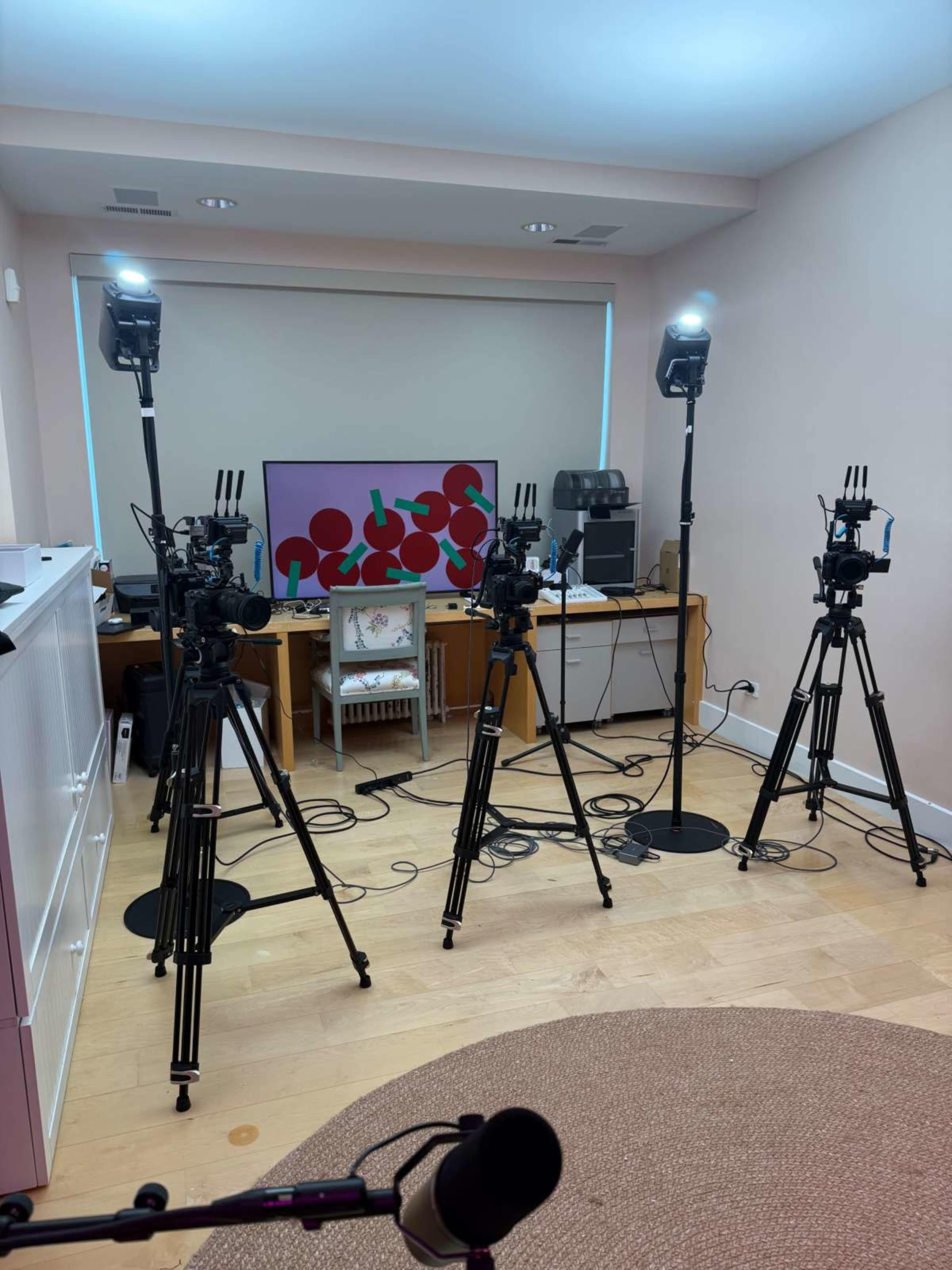 The image shows a well-lit room with four cameras on tripods facing a television displaying colorful graphics.