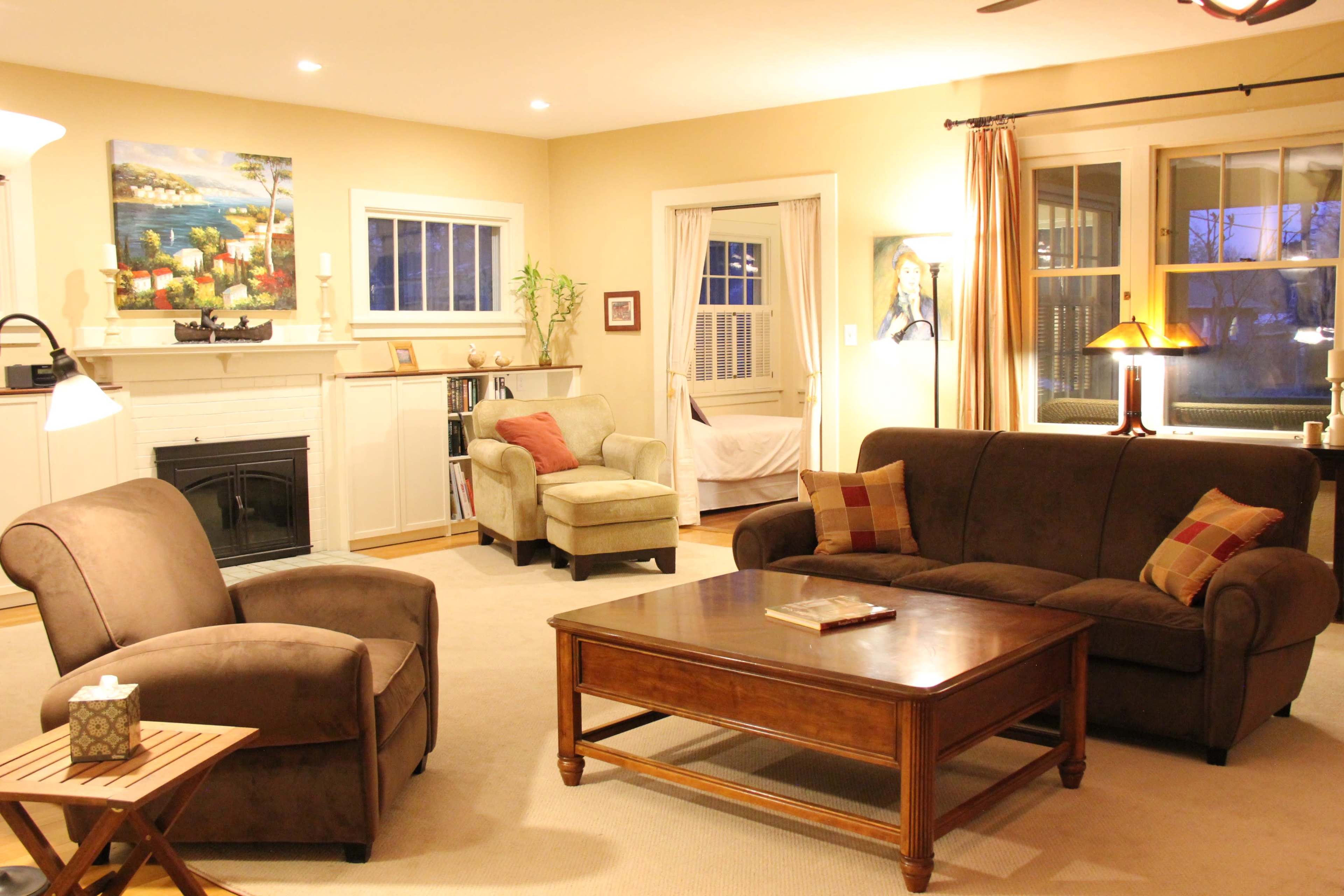 A well-furnished living room featuring a brown sofa, a beige armchair, a wooden coffee table, and a fireplace with artwork on the walls.
