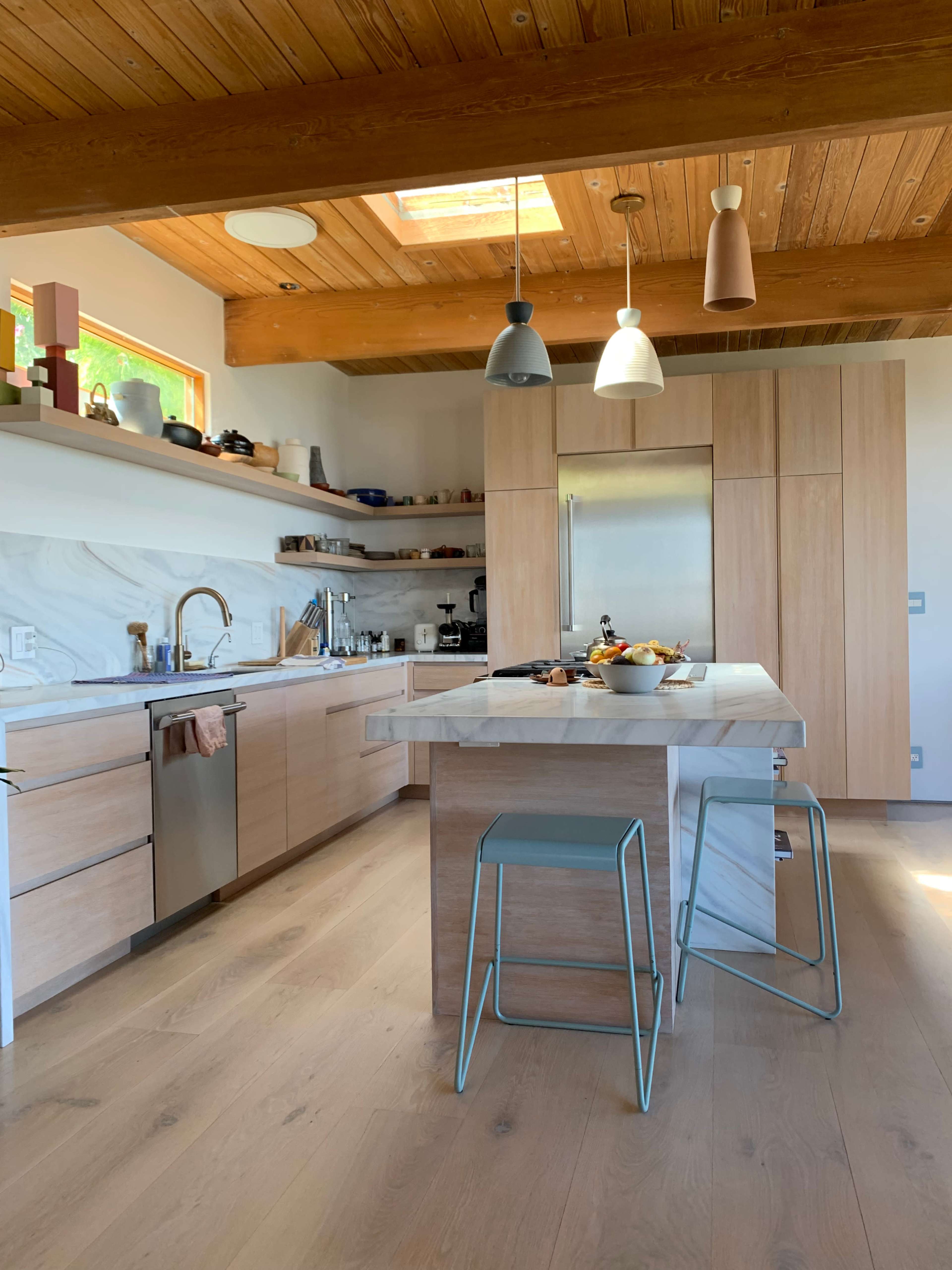 The kitchen features wooden beams, a central island with modern stools, and light-colored cabinetry with a marble accent.