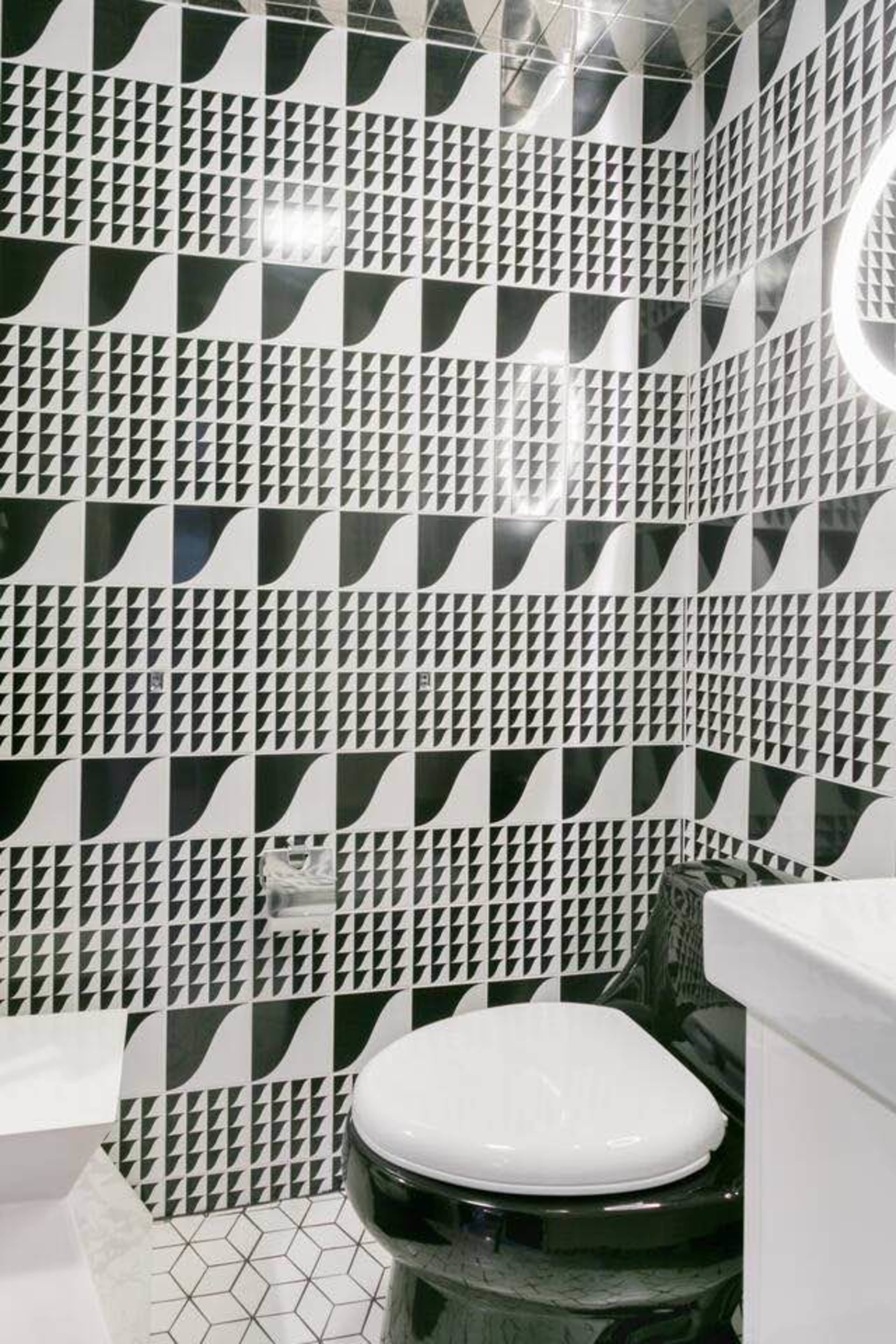 A small bathroom featuring a black and white patterned tile wall and a black toilet with a white seat.