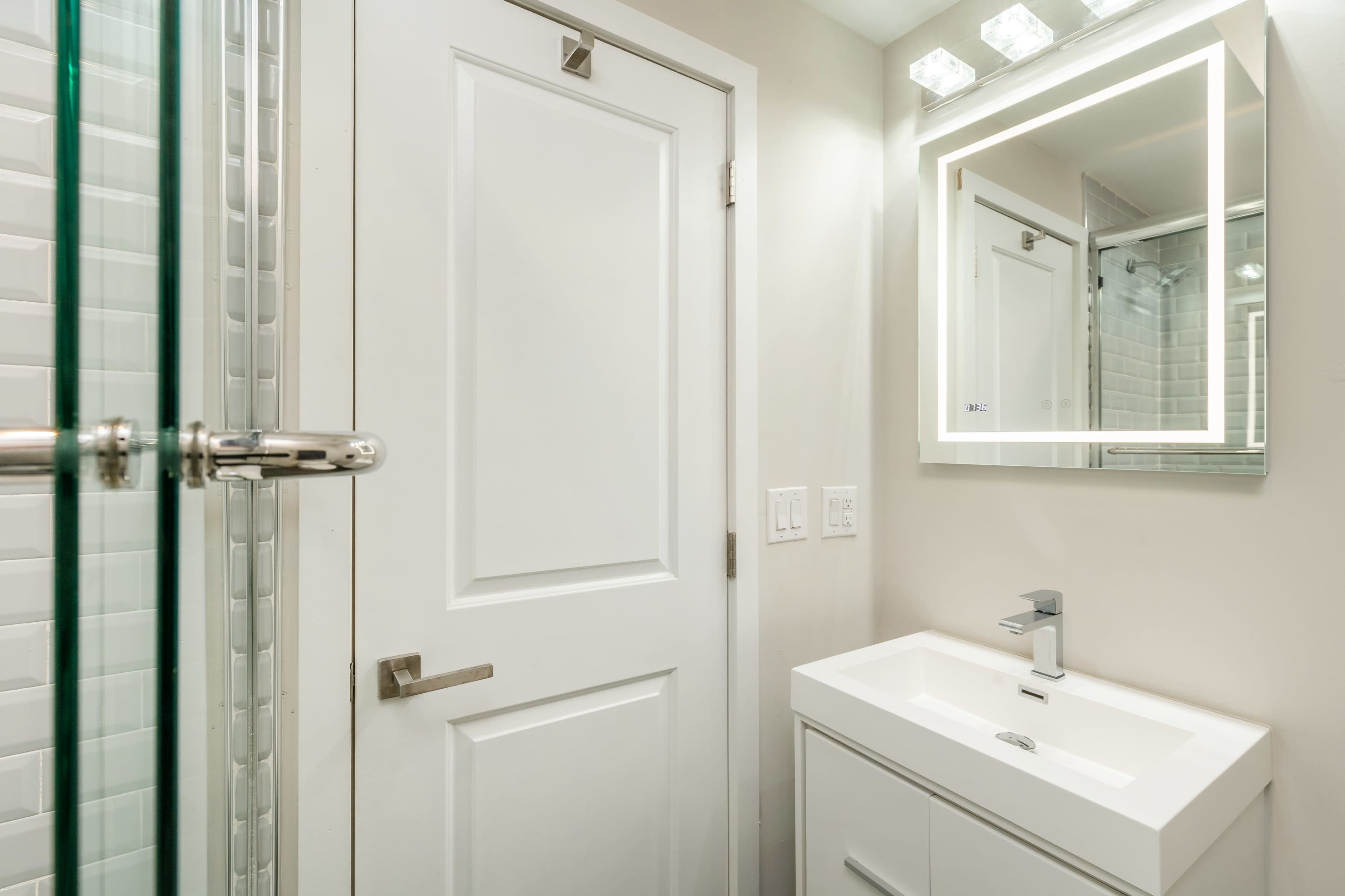 A modern bathroom featuring a white vanity with a sink, a large mirror, and a shower enclosed by glass panels.