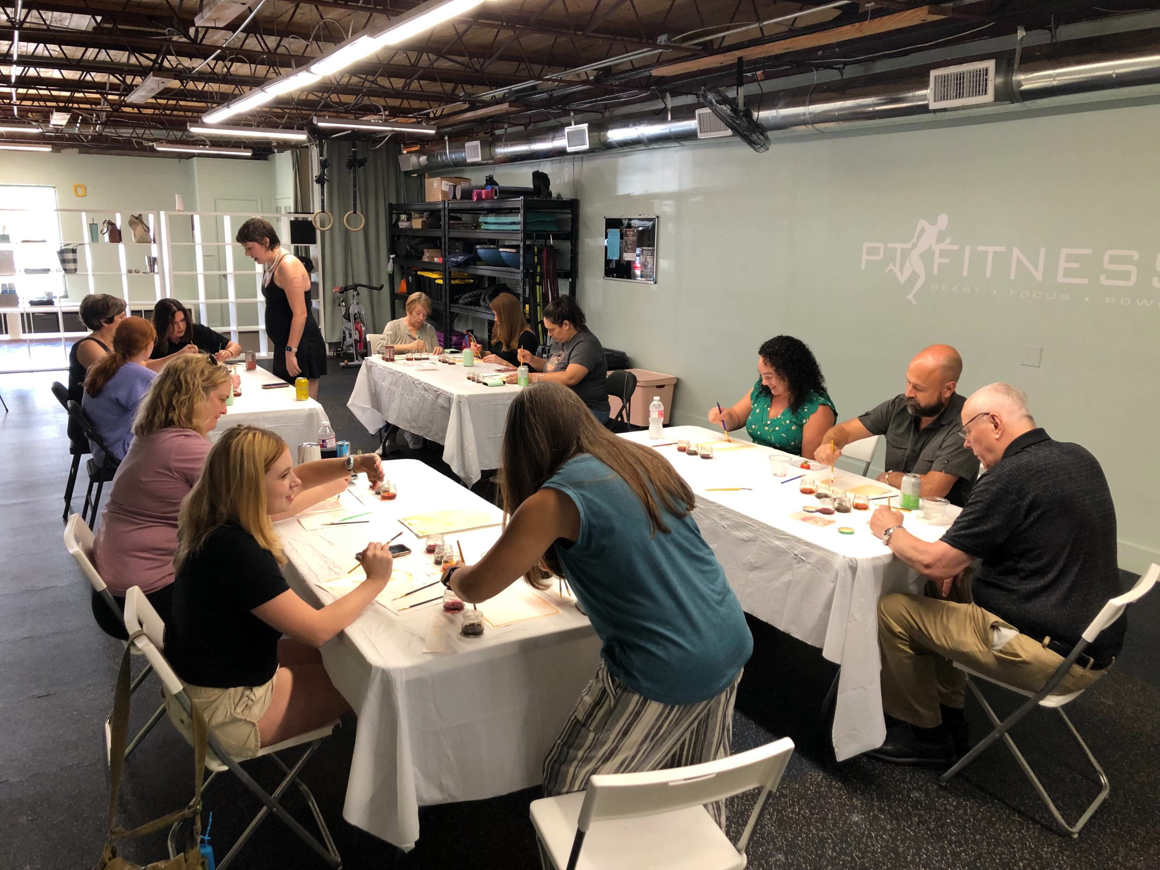 A group of people is engaged in a painting activity at tables in an indoor space.