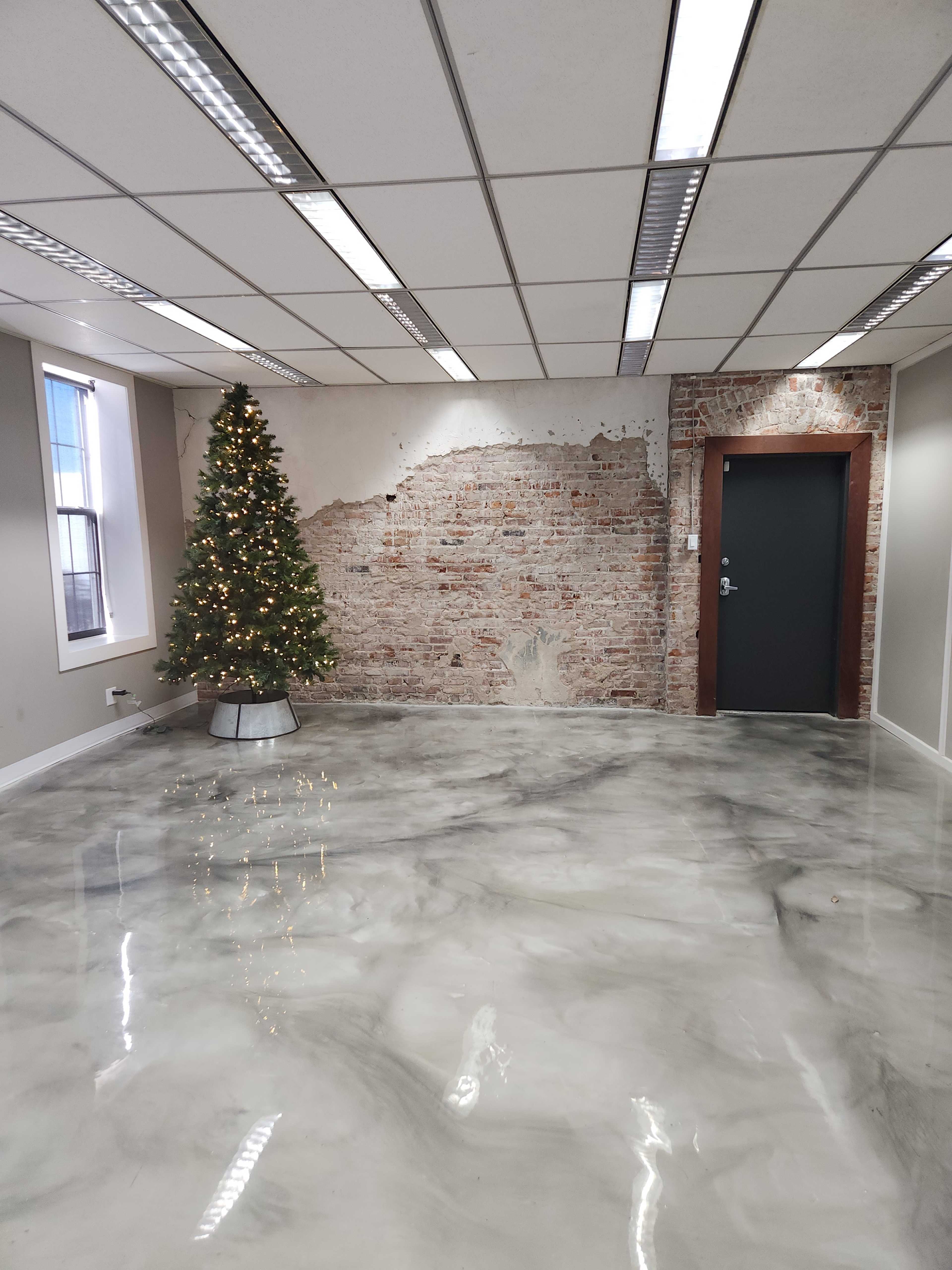 An empty office space with a Christmas tree in one corner, a partially exposed brick wall, and a smooth, glossy floor.