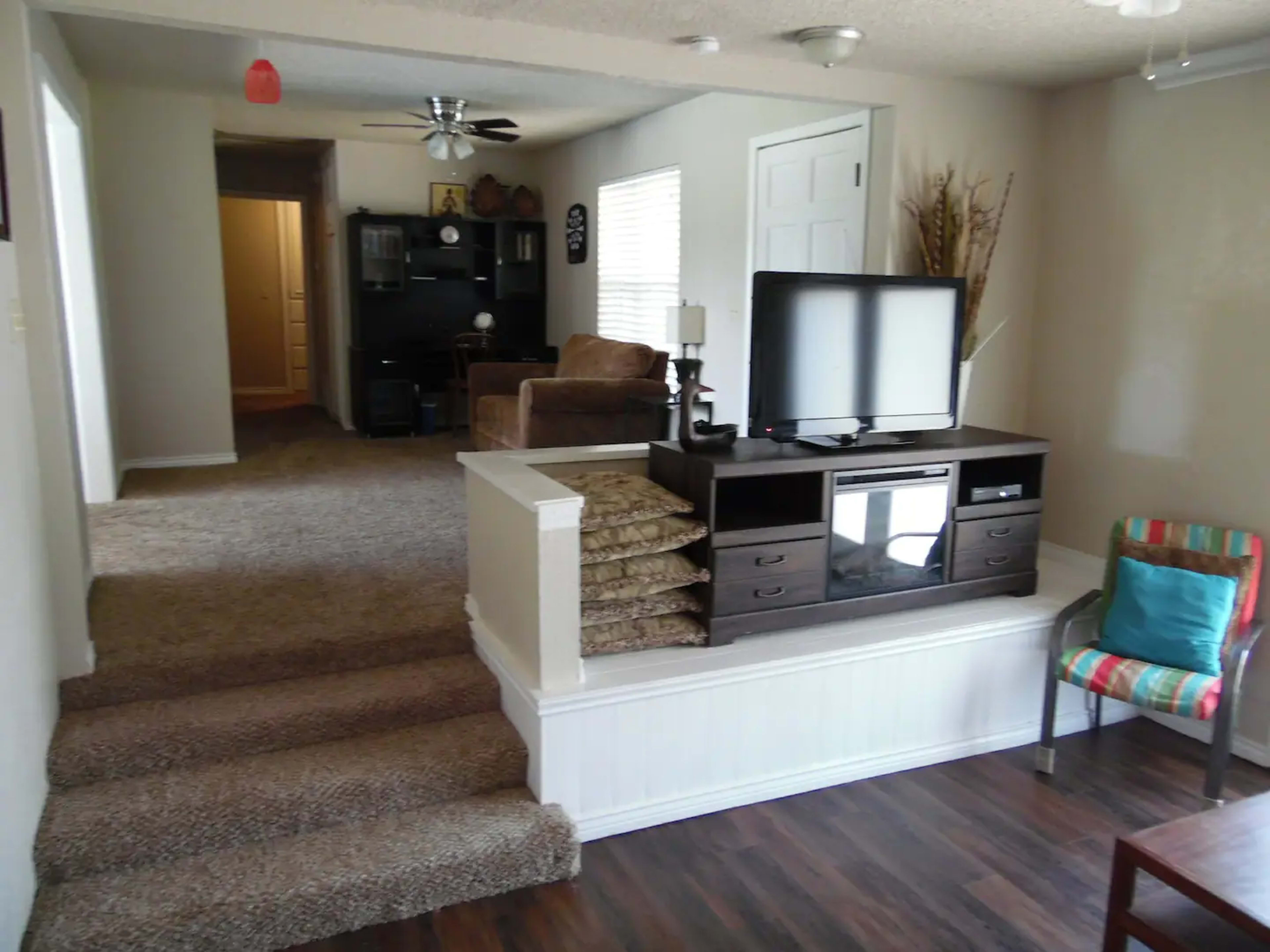 A living space with a television on a console table, steps leading to a carpeted area, and a small chair next to a decorative piece.