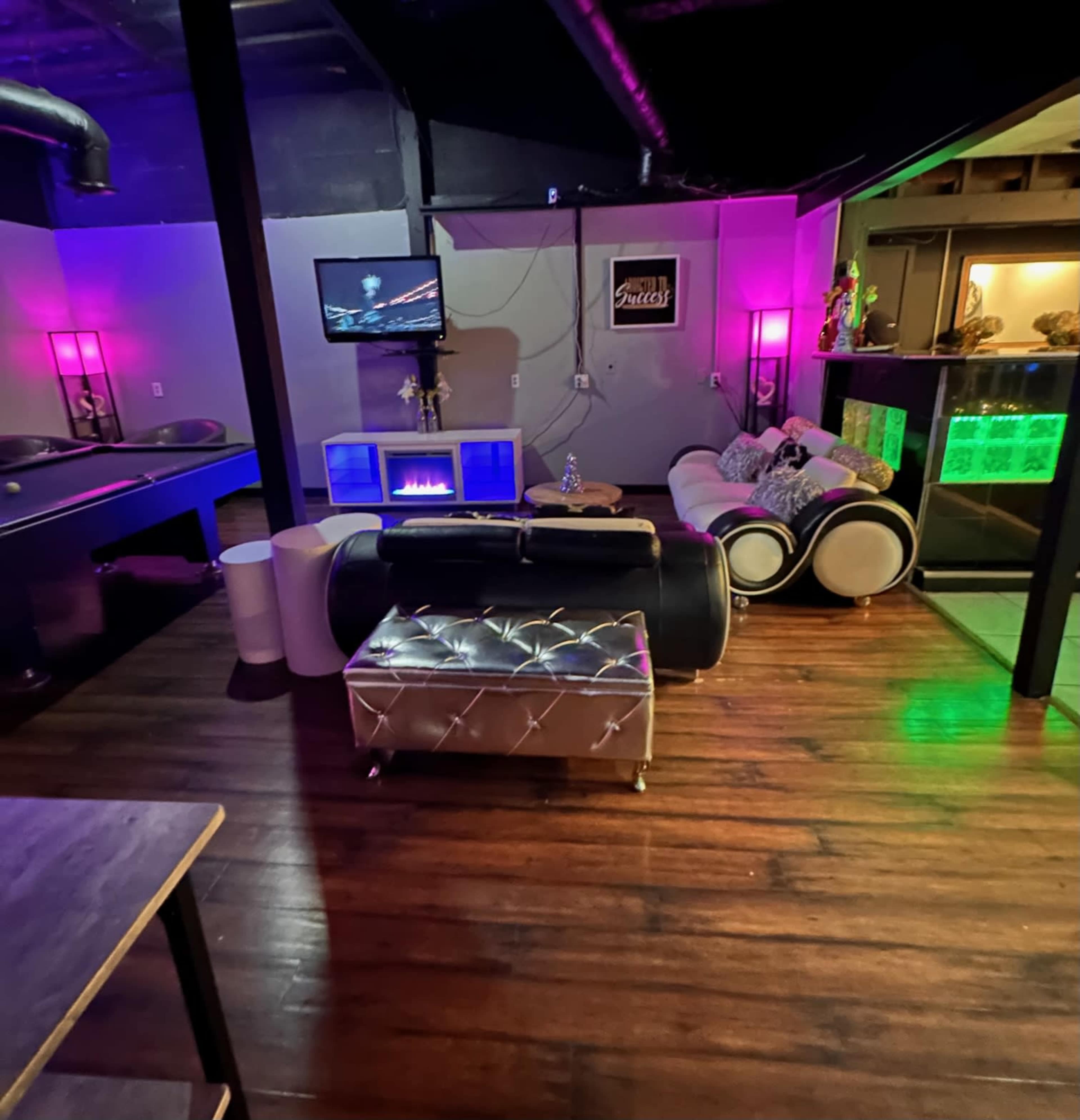A modern lounge area with sleek furniture, a large TV mounted on the wall, and ambient lighting in purple and green.