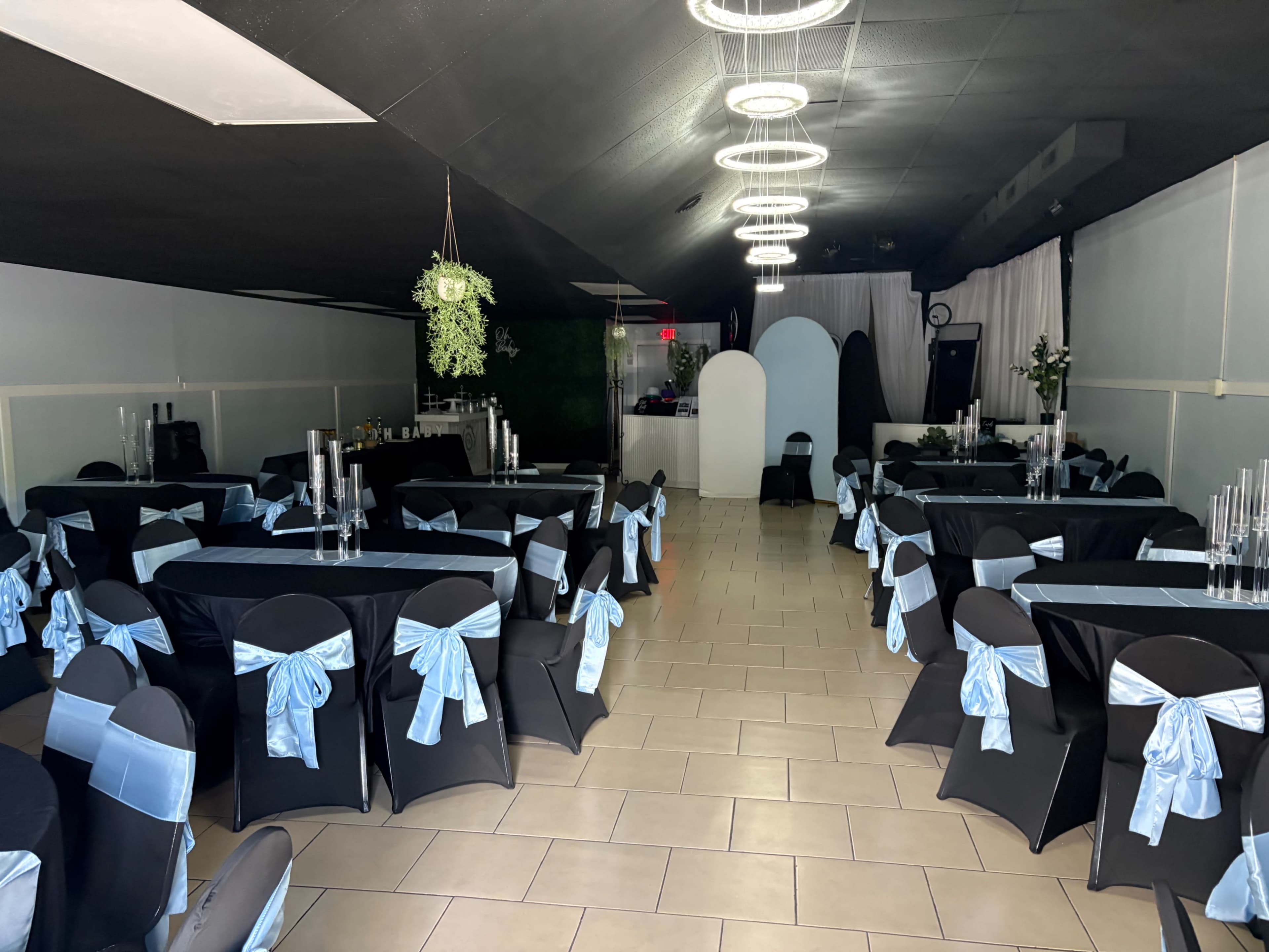 The image shows a banquet hall set up with black tables adorned with light blue bows and tall candle holders, creating a formal dining arrangement.
