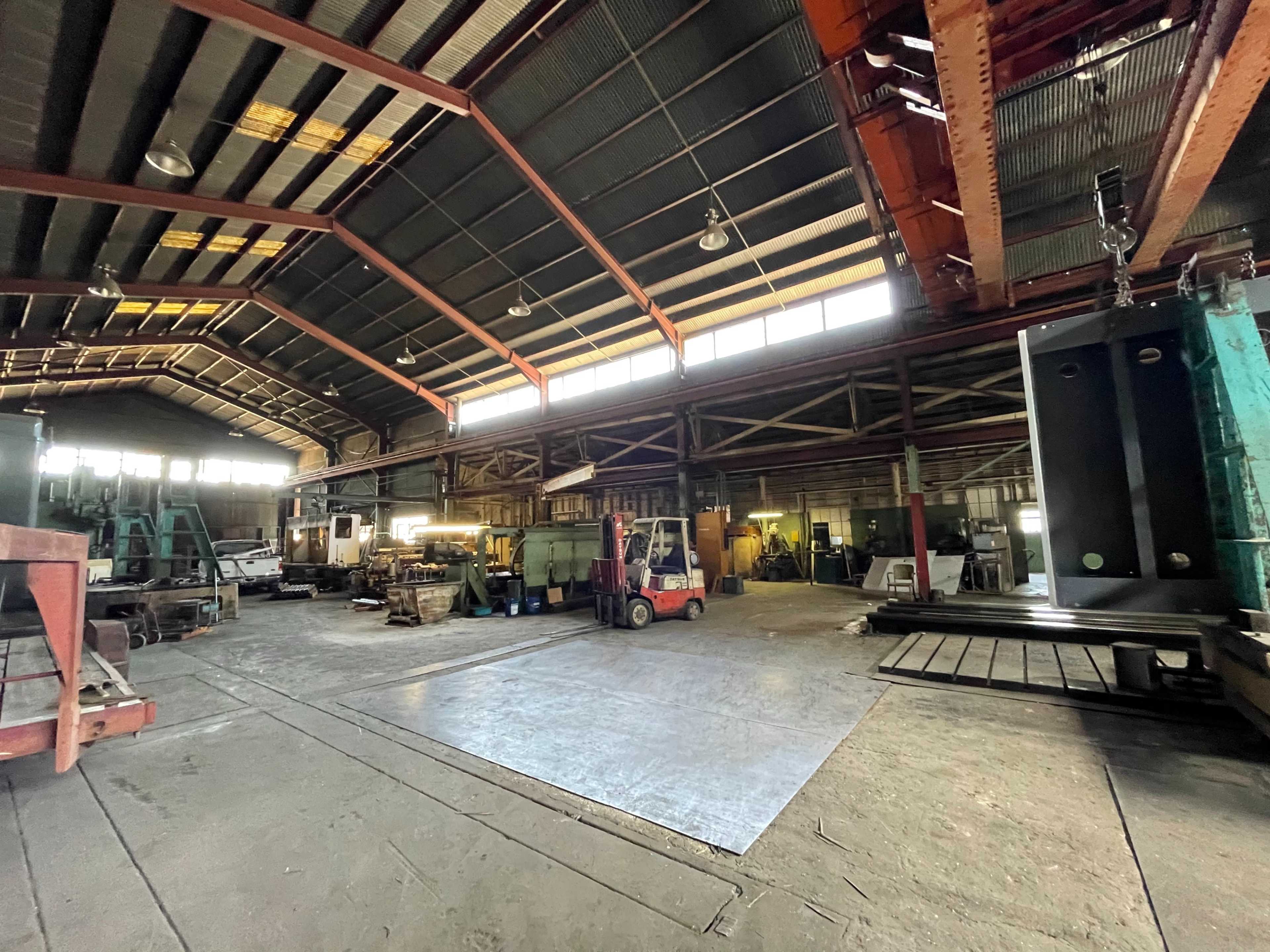 The image shows a large industrial workshop with various machinery and equipment arranged throughout the space under a high ceiling.