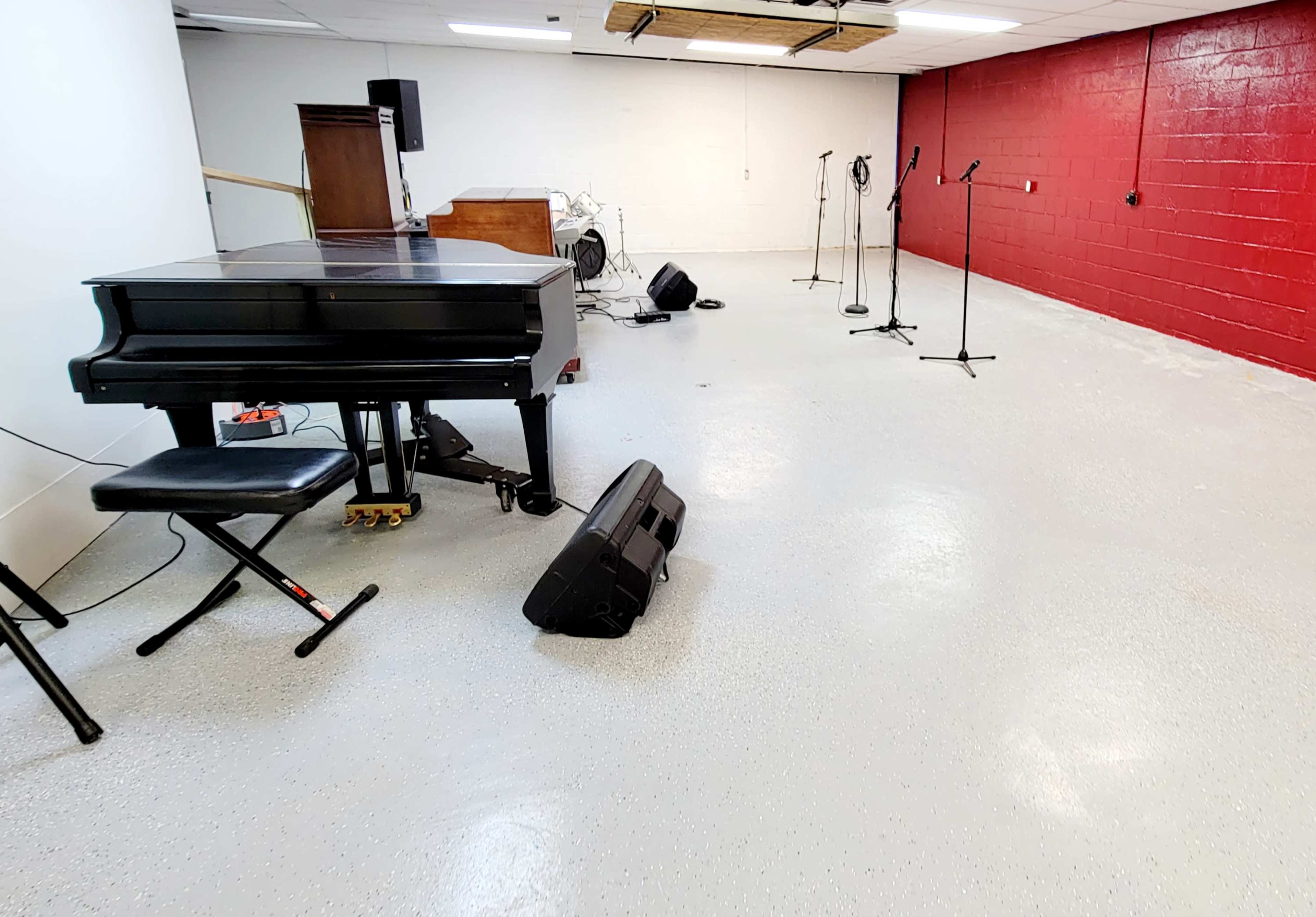 A spacious room with a black piano, several microphones on stands, and a few speakers placed on the floor.