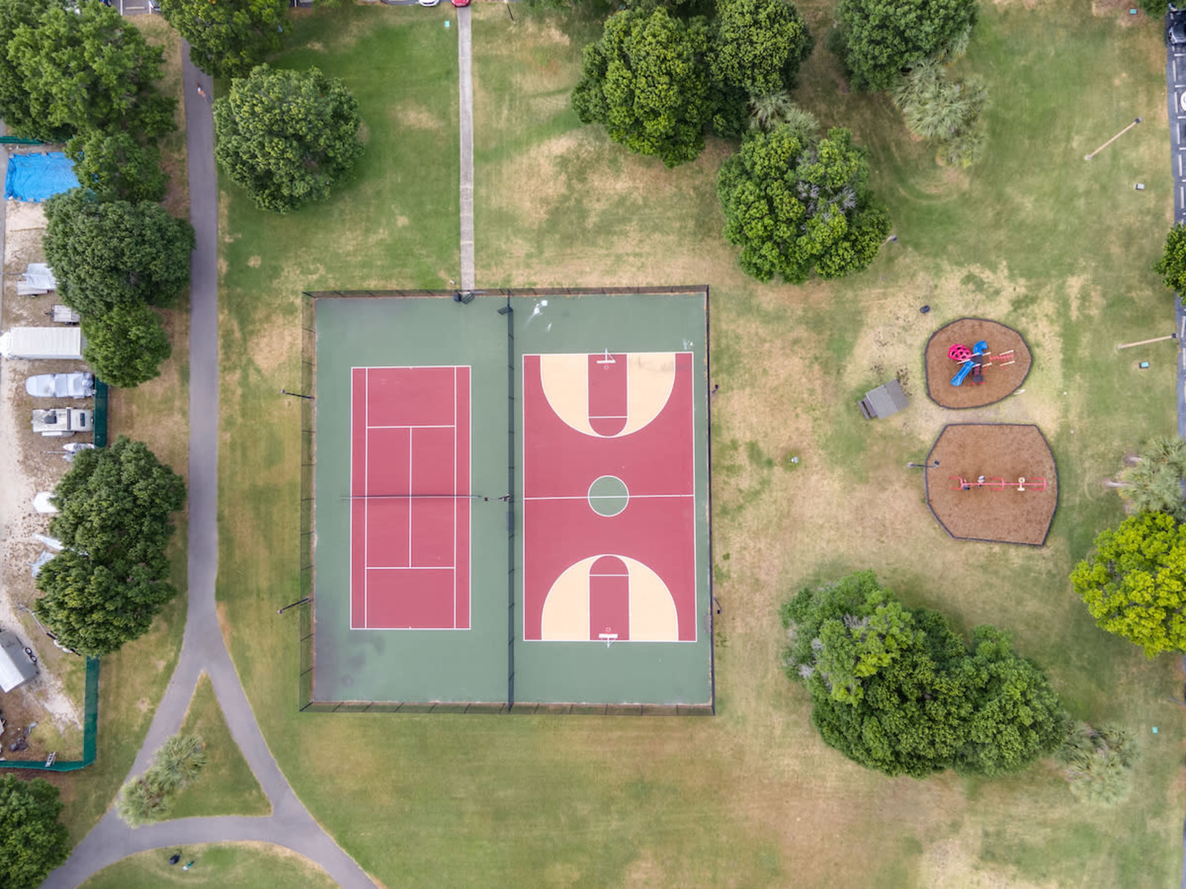 An aerial view of two basketball courts and a playground surrounded by trees and grass.