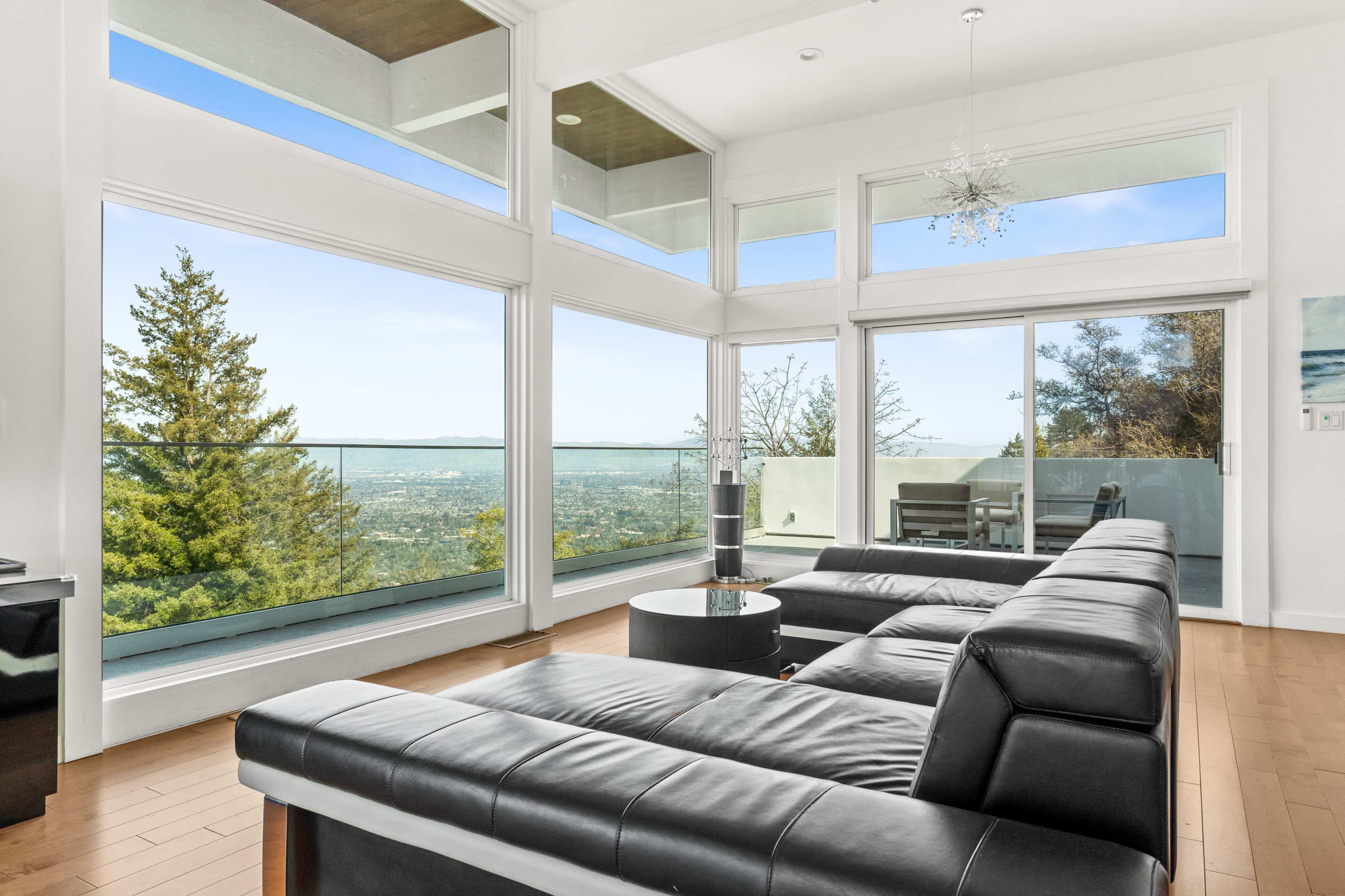 A modern living room features large windows showcasing a mountain view and sleek furniture arranged around a circular coffee table.