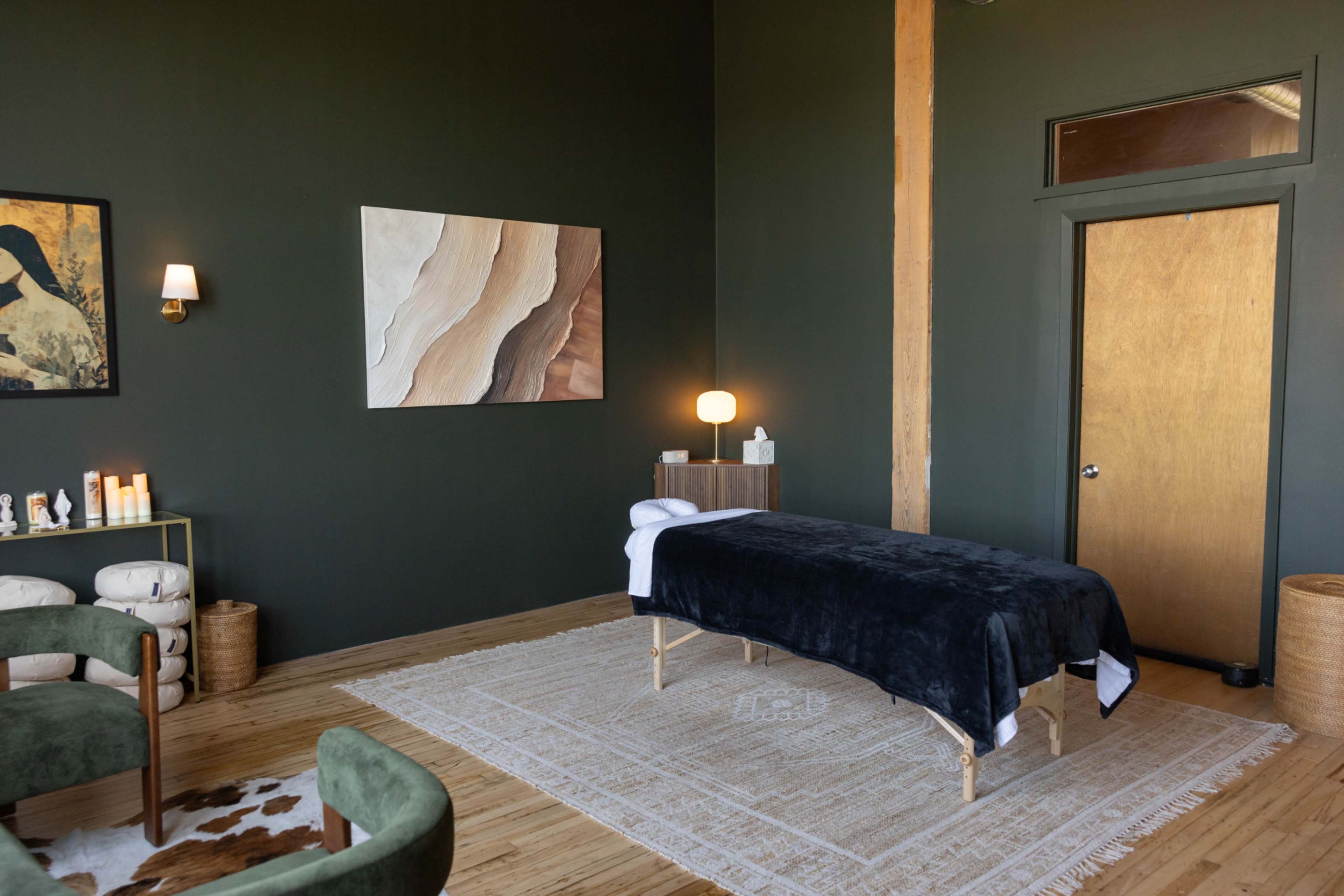 The image shows a serene massage room featuring a massage table, art on the walls, and modern decor elements.