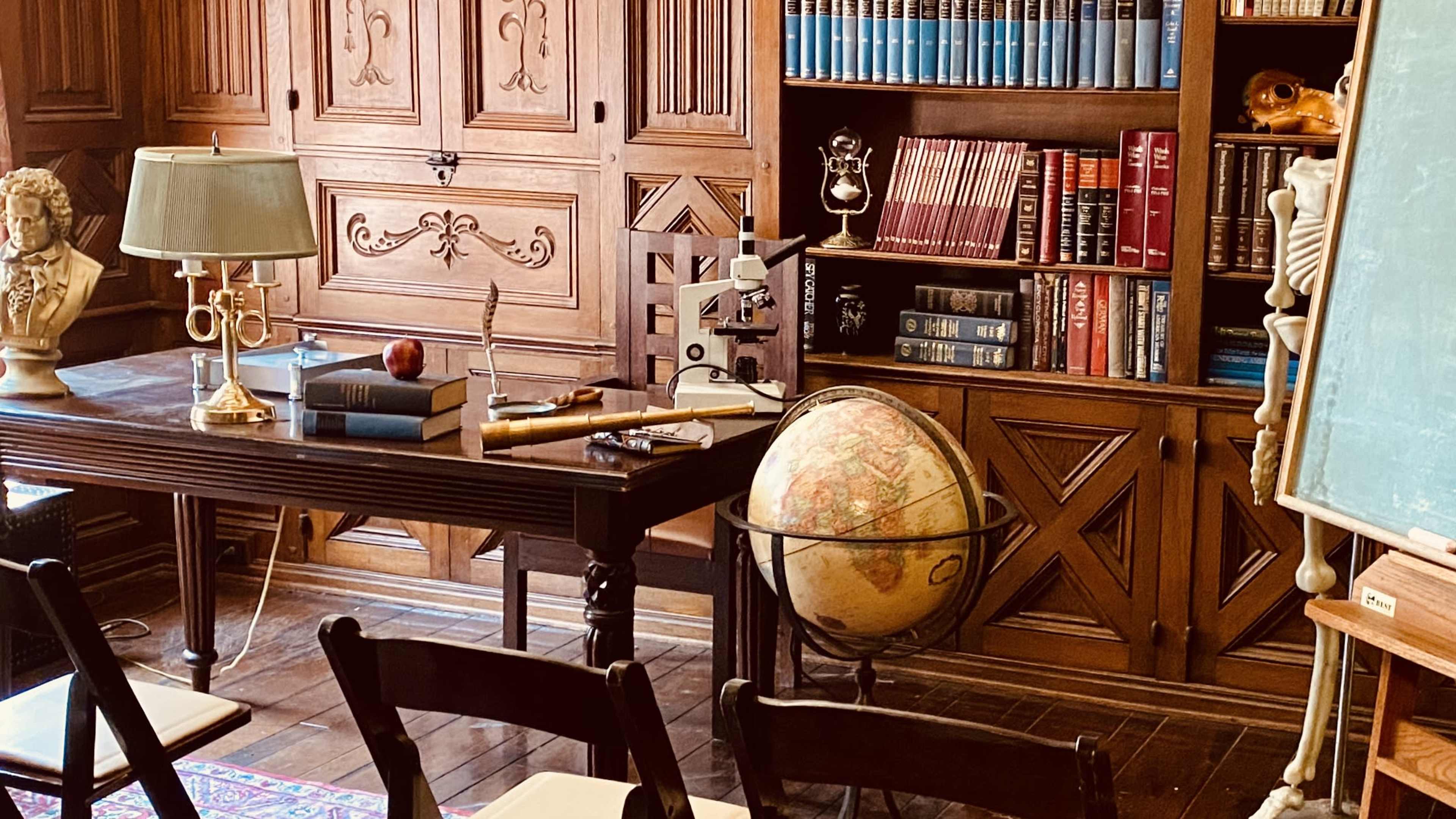 A classic study room with a wooden desk, a globe on a stand, bookshelves filled with books, and various study materials arranged on the desk.