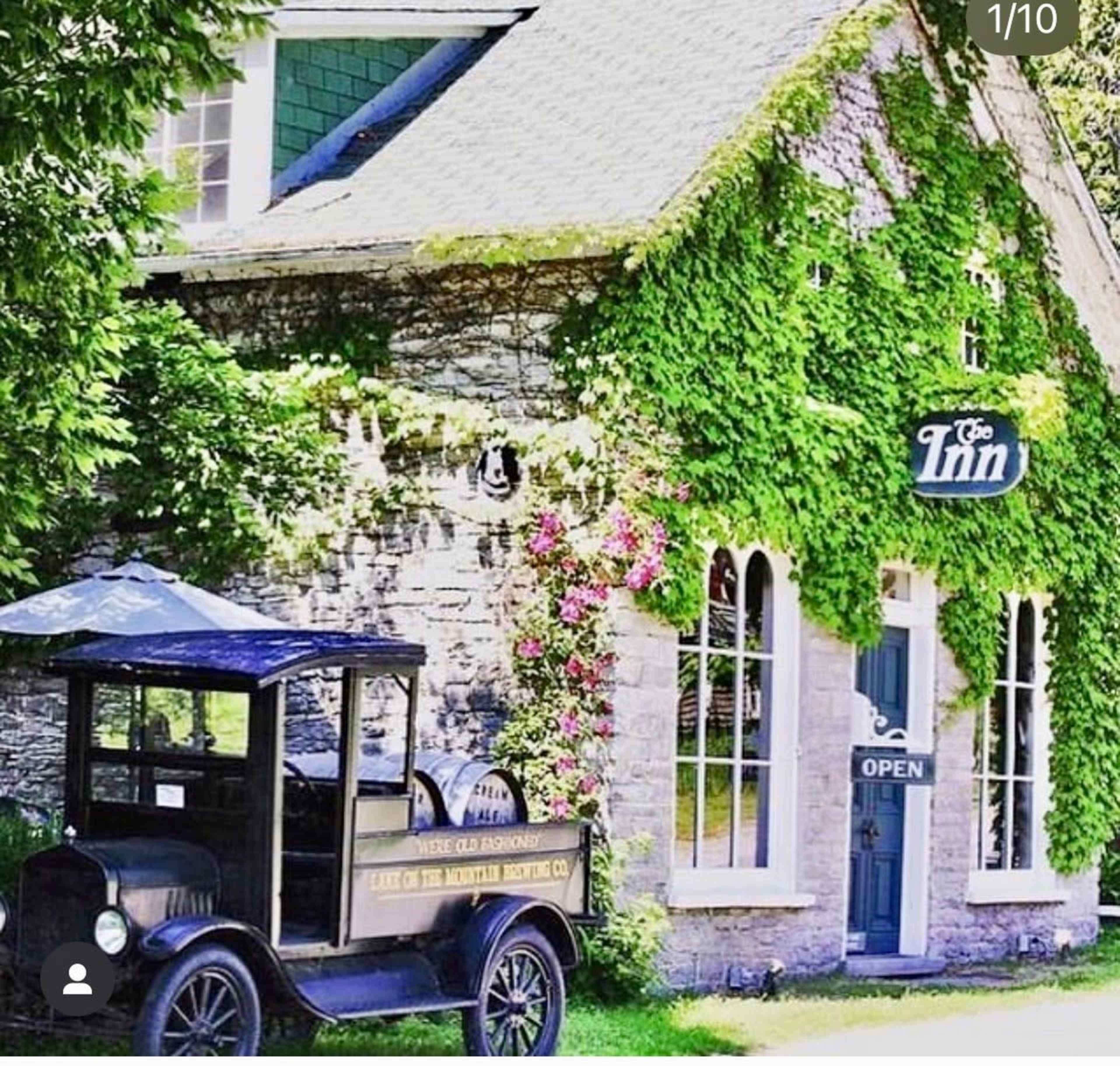 A vintage truck is parked outside a stone building covered in green ivy, with the sign "The Inn" and an "Open" sign visible on the door.
