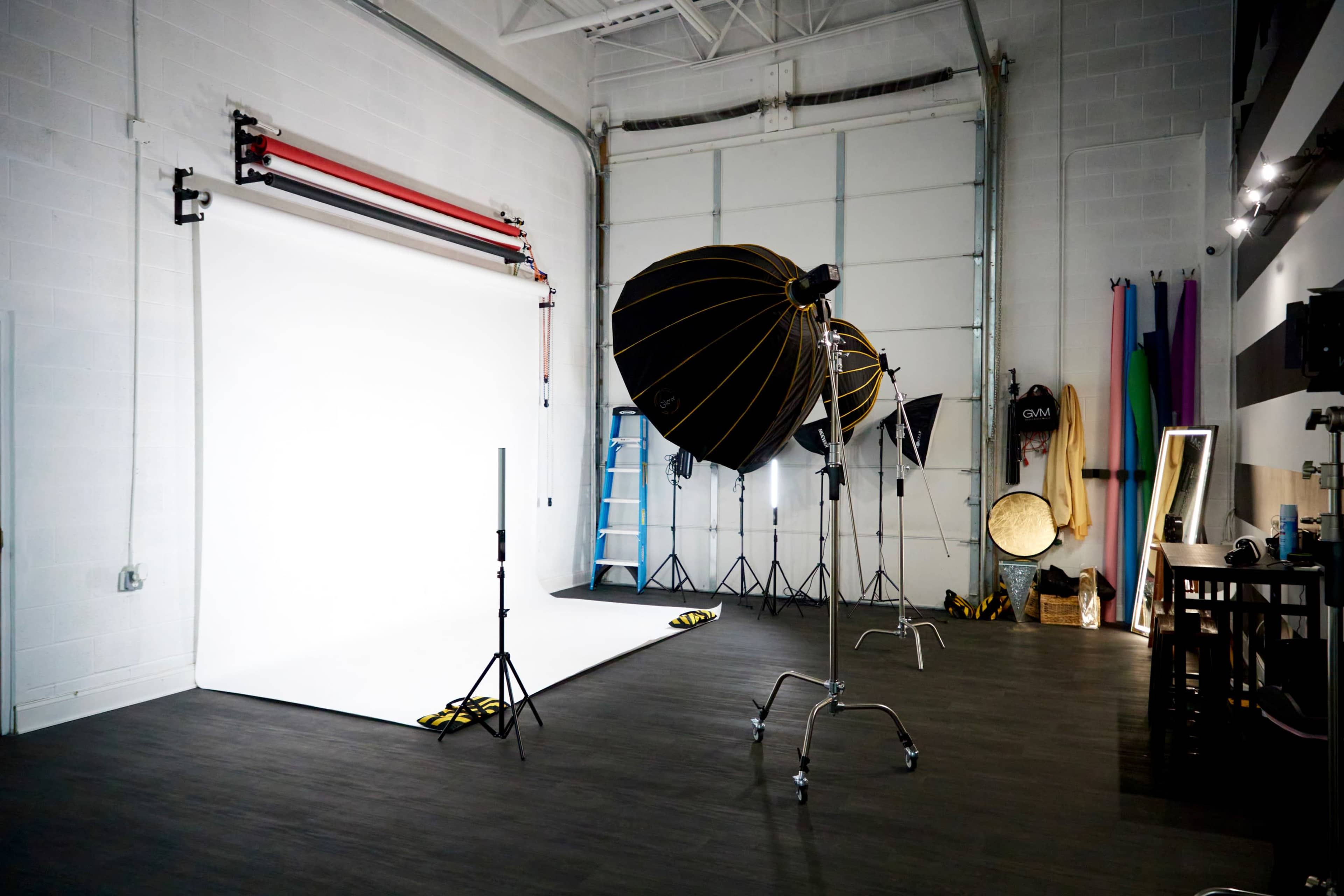 A photography studio equipped with a white backdrop, lighting setups, and various props along the walls.