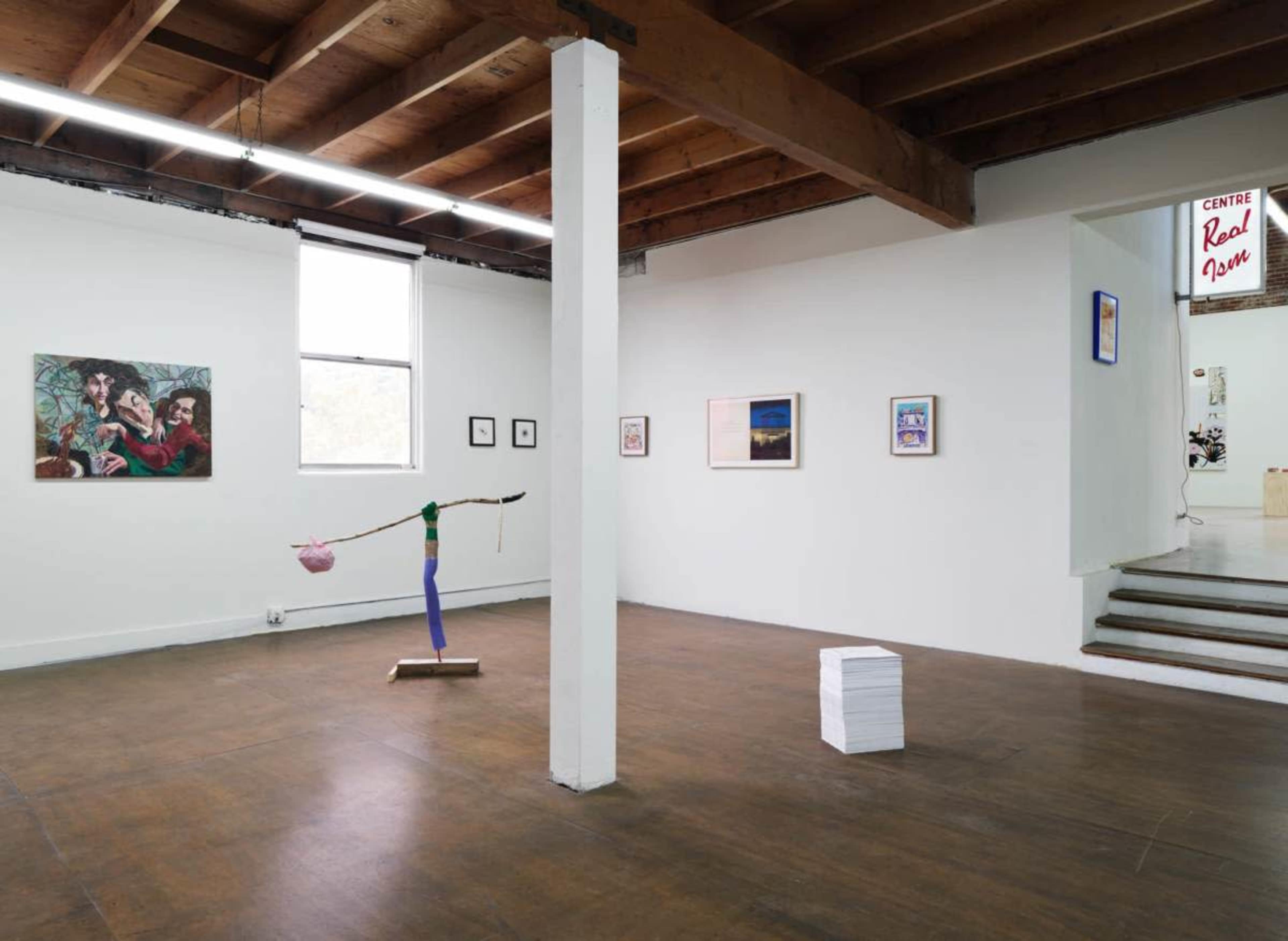 An art gallery with a wooden ceiling, featuring various framed artworks on the walls and a colorful sculpture in the center of the room.