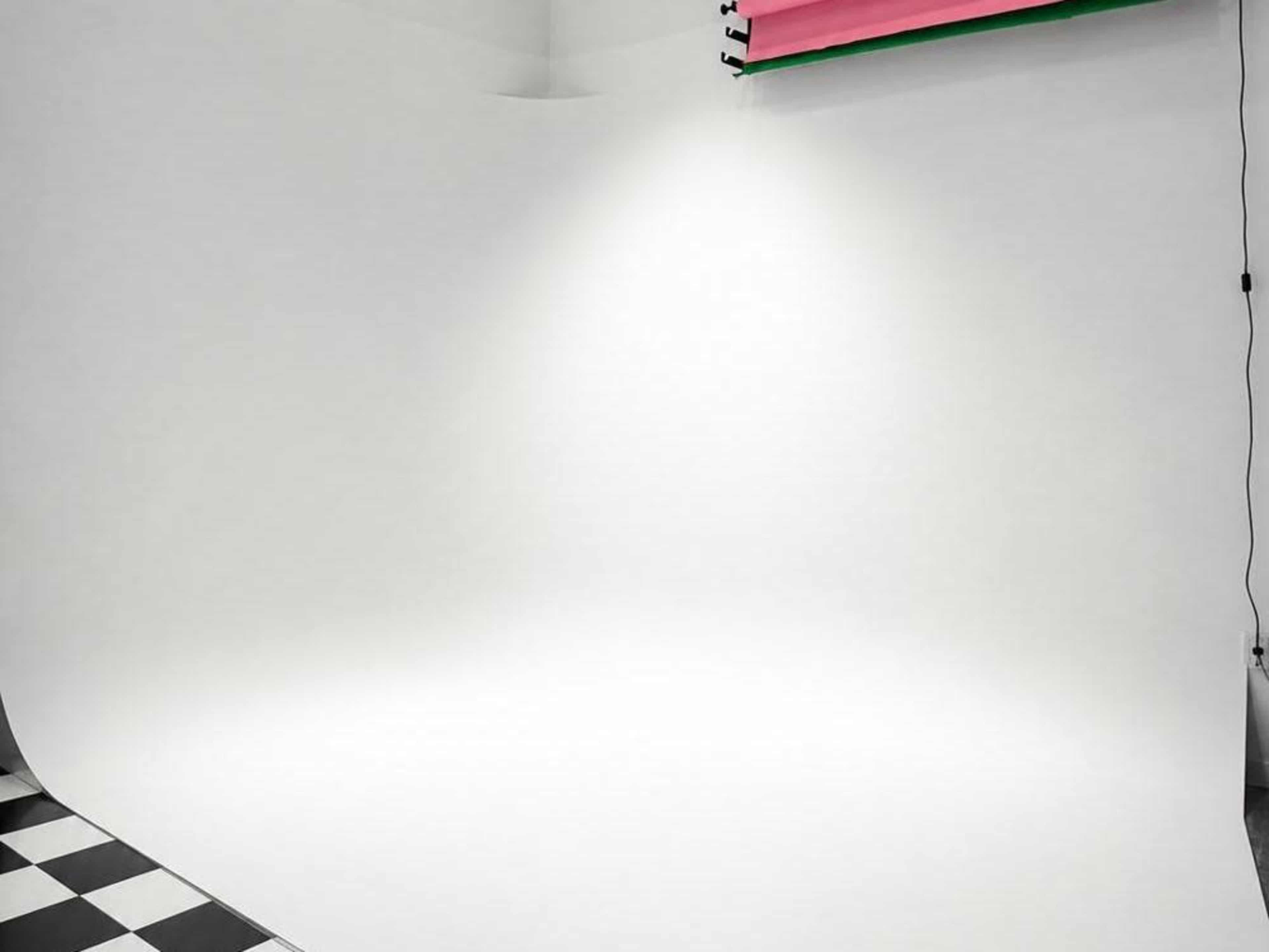The image shows a photography studio with a smooth white backdrop and checkered flooring.