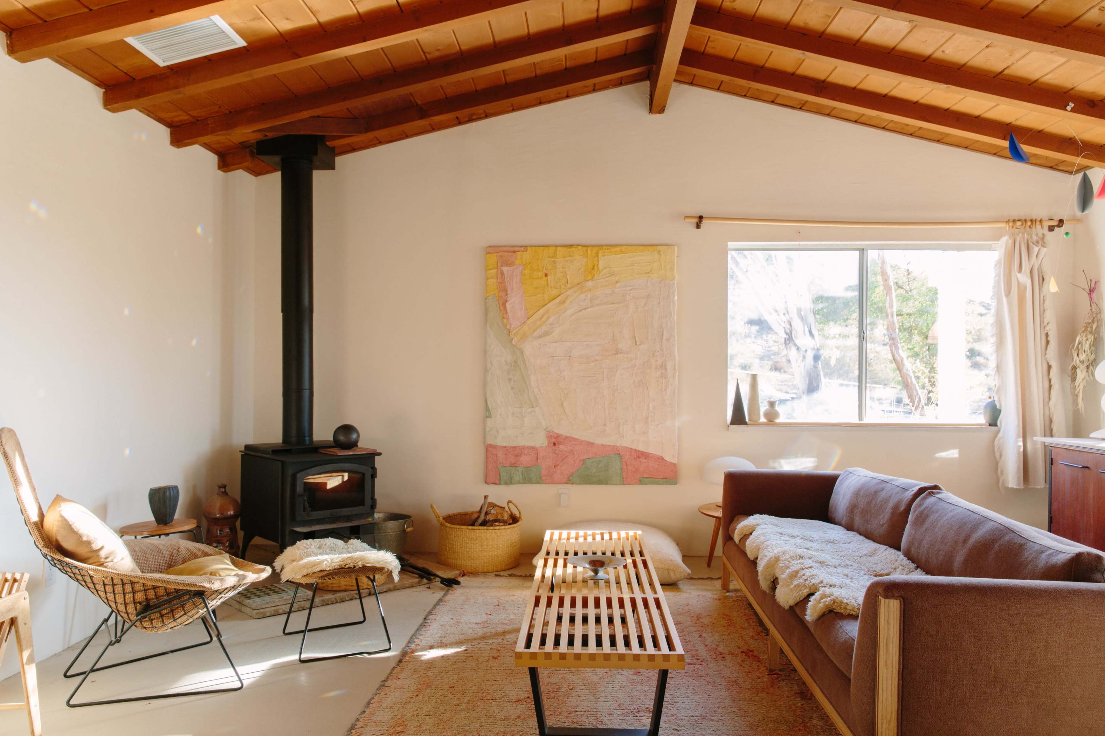 A cozy living room featuring a wood-burning stove, a large abstract painting, a wooden ceiling, and a seating area with a sofa and two chairs.