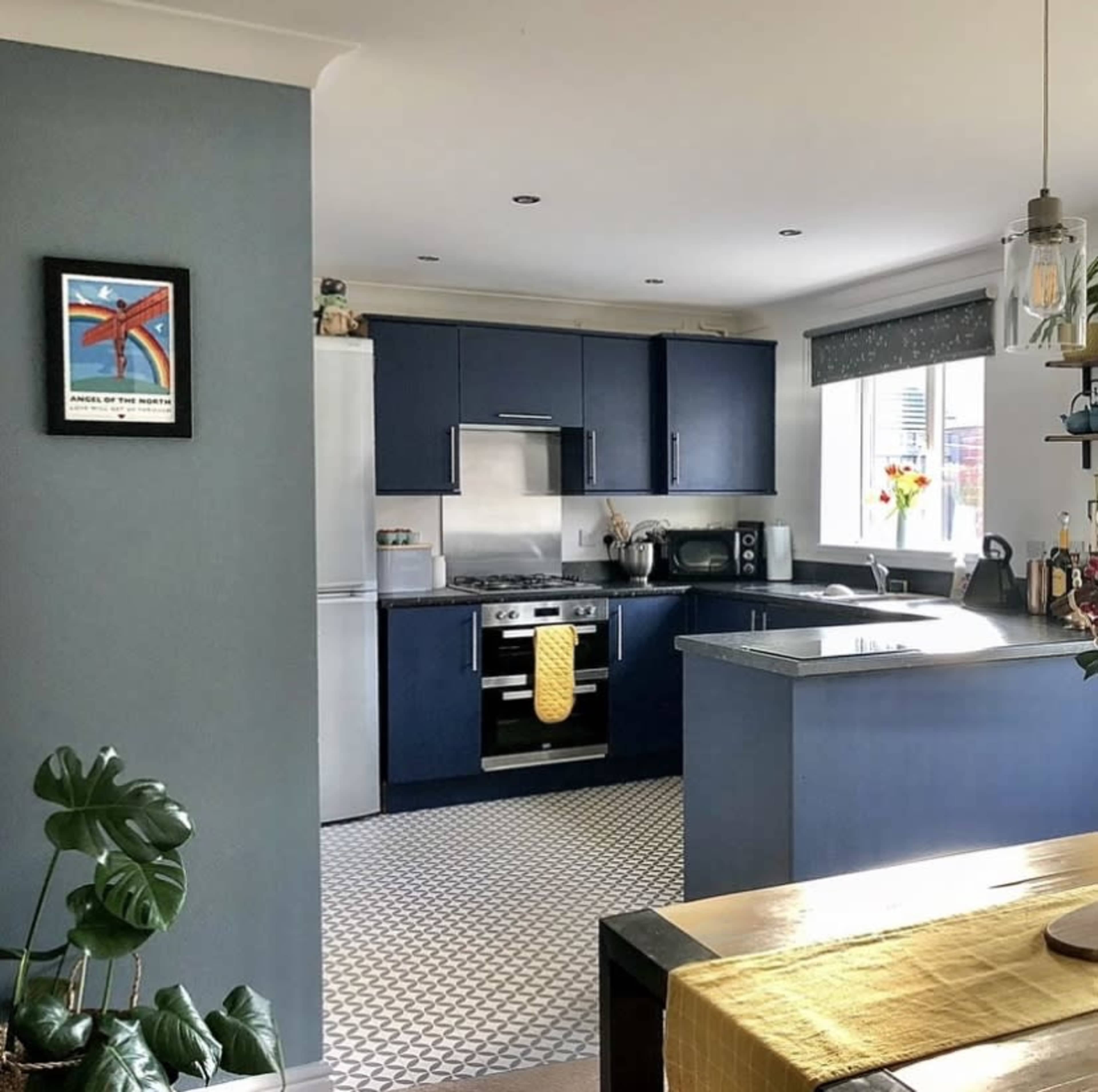 A modern kitchen with navy blue cabinets, a silver stove, and a patterned floor, along with a dining area featuring a yellow tablecloth.