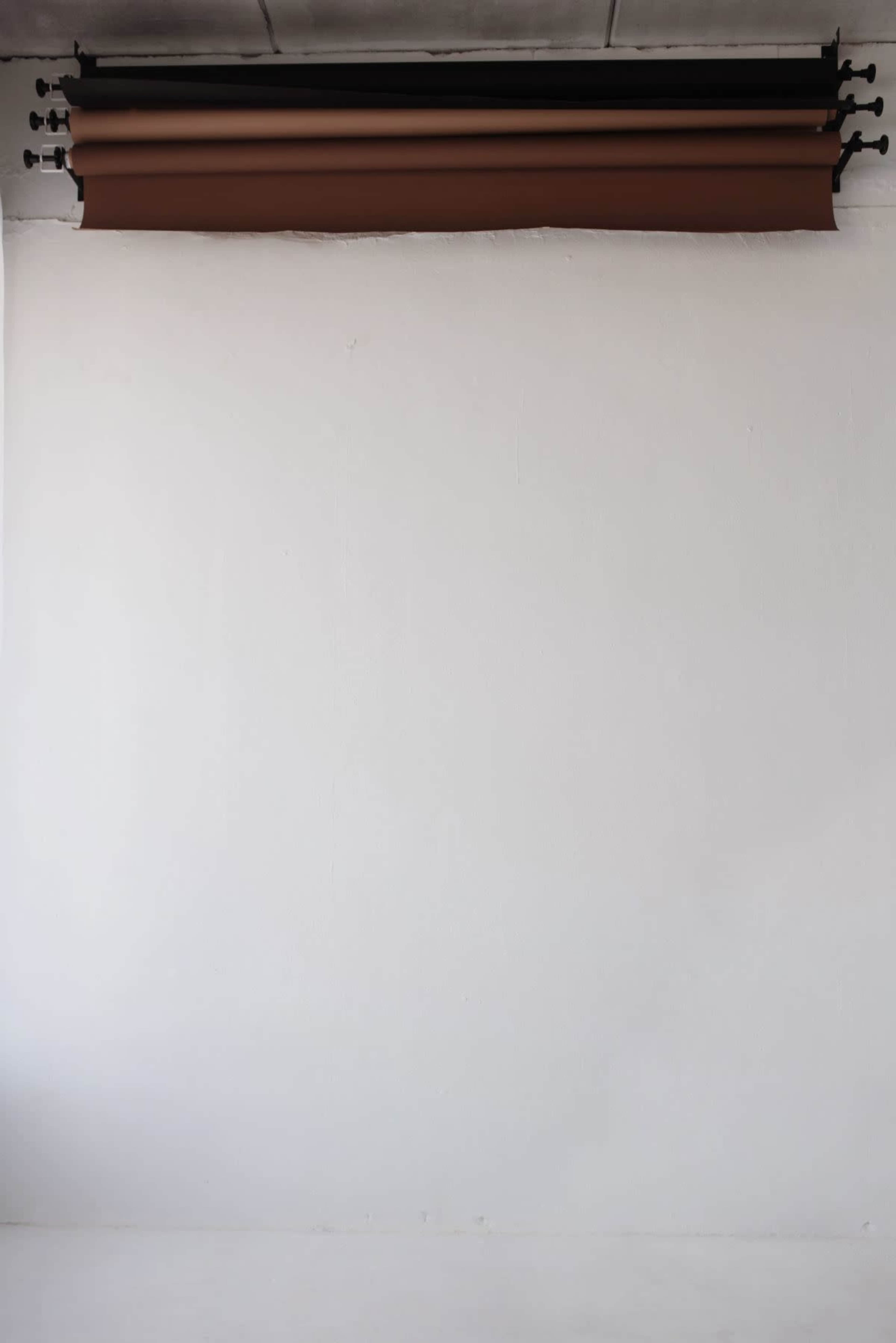 A smooth white wall features rolls of brown backdrop paper mounted above it.