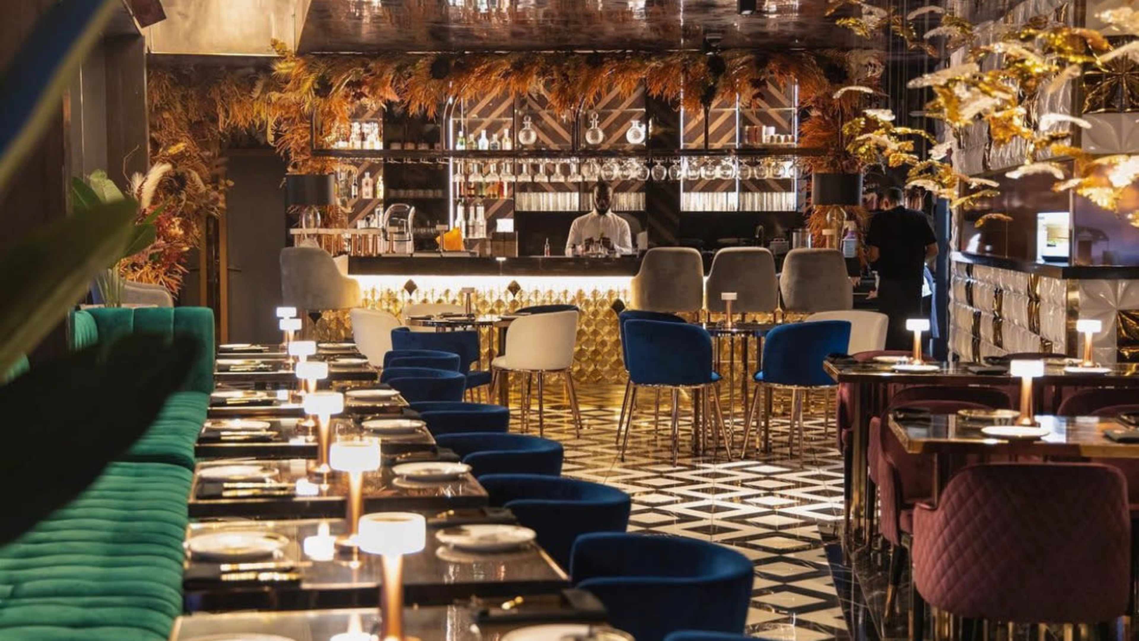 The image shows a stylish restaurant interior featuring a bar area with a modern design, surrounded by tables with elegant seating.