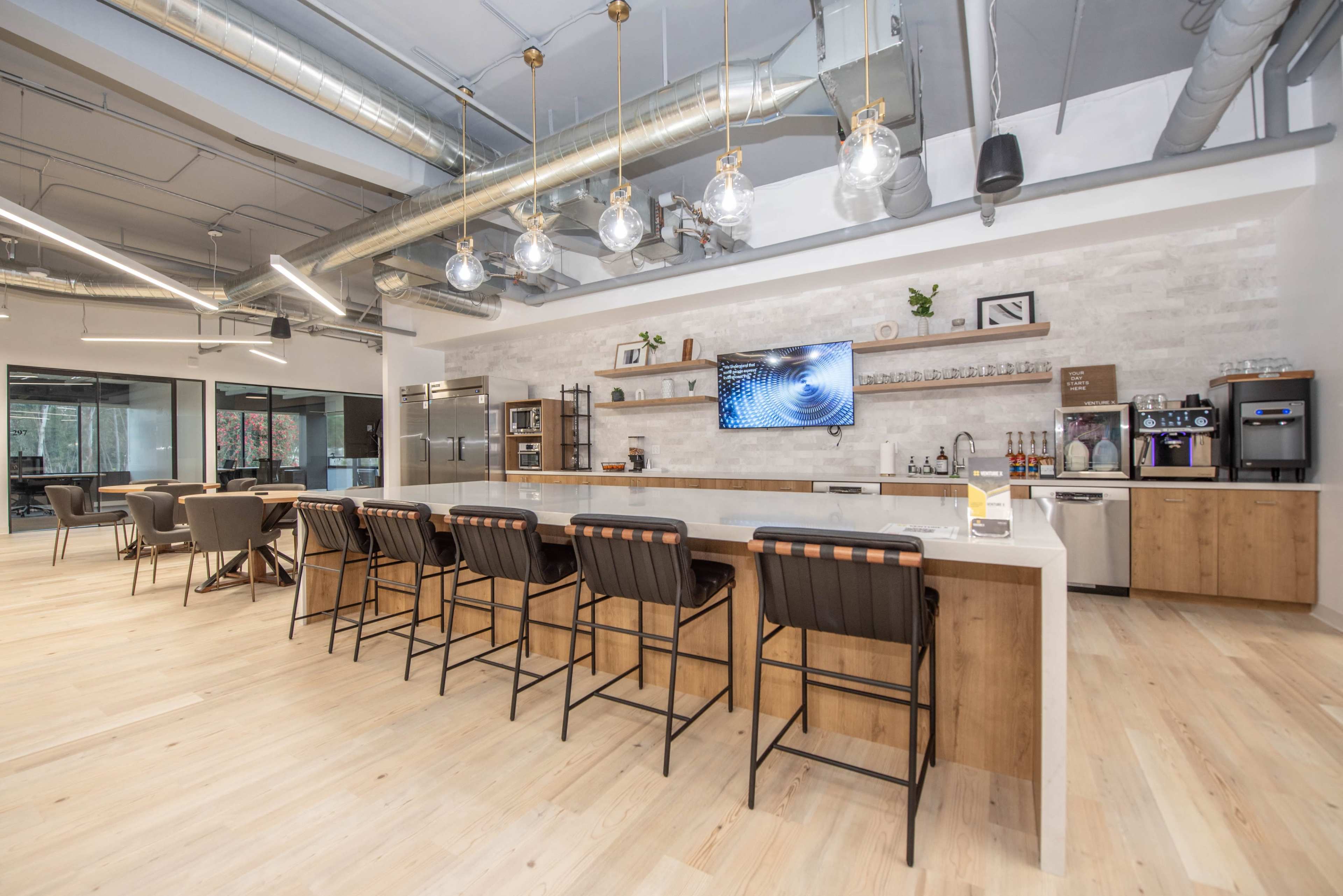 A modern kitchen area with a long countertop, bar seating, and various kitchen appliances on display against a light-colored wall.