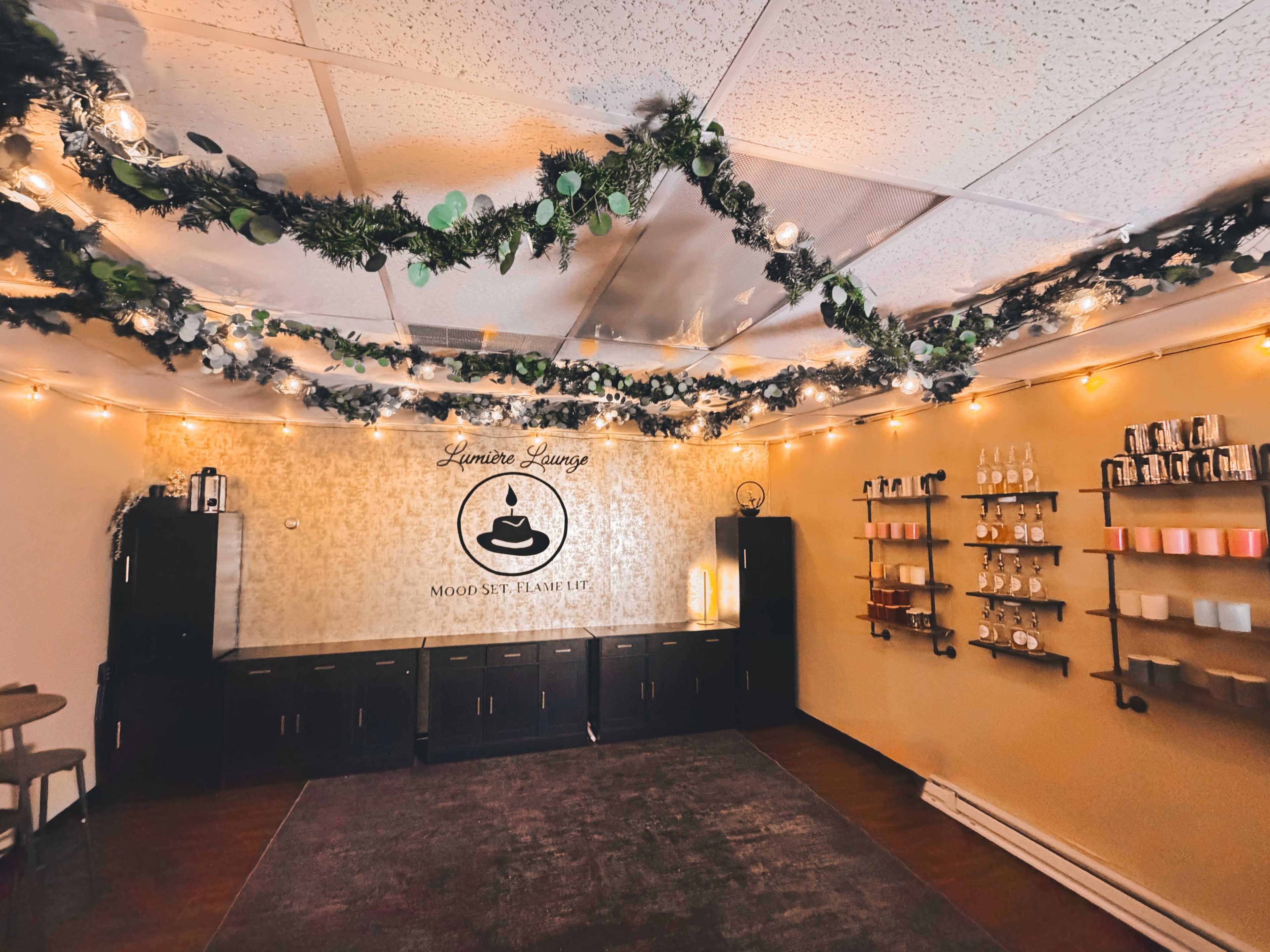 The image shows a cozy lounge decorated with string lights and greenery, featuring a wall with the name "Luminite Lounge" and shelves displaying various items.