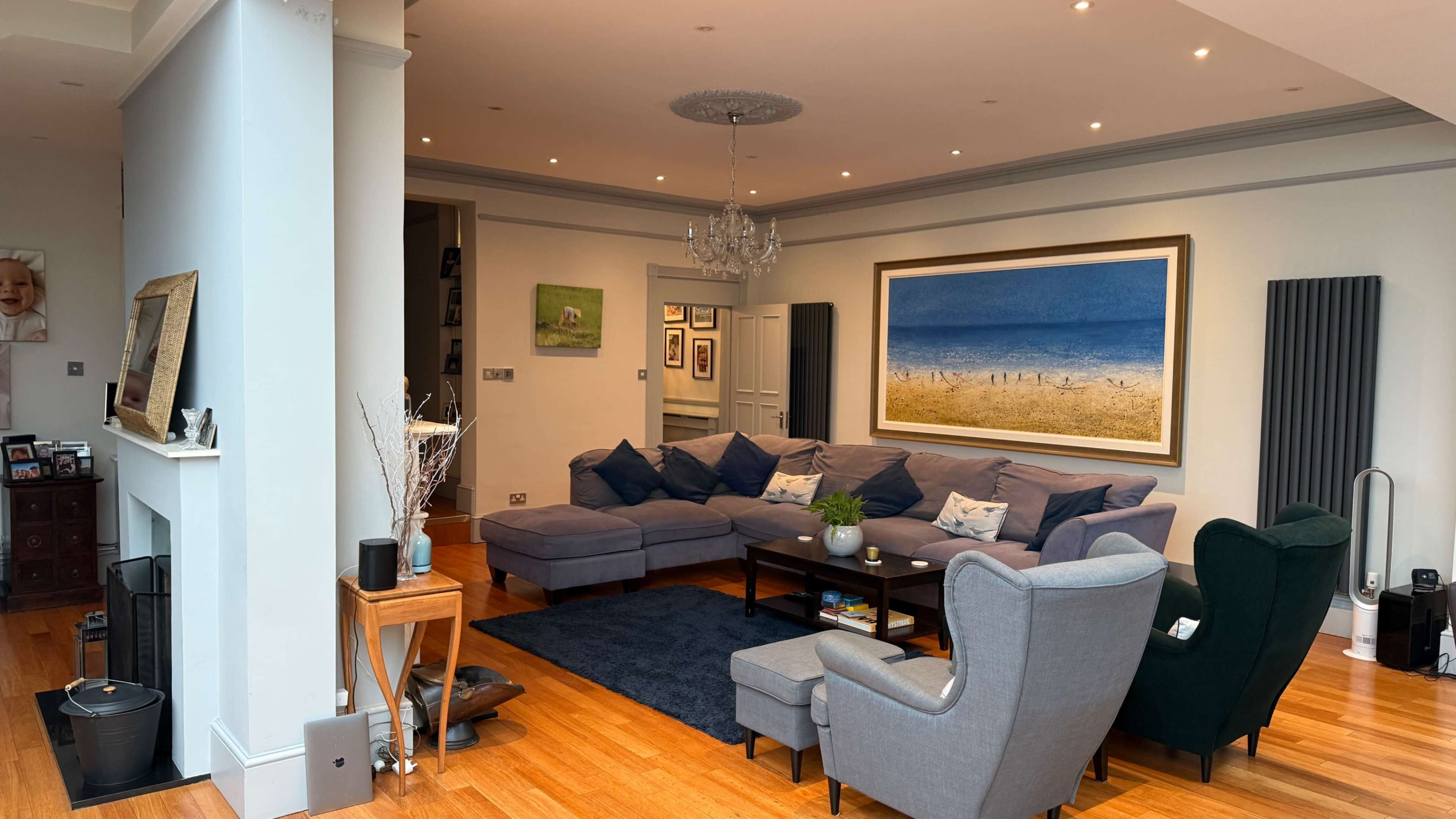 The living room features a large gray sectional sofa, a light blue area rug, and a prominent artwork depicting a beach scene on the wall.