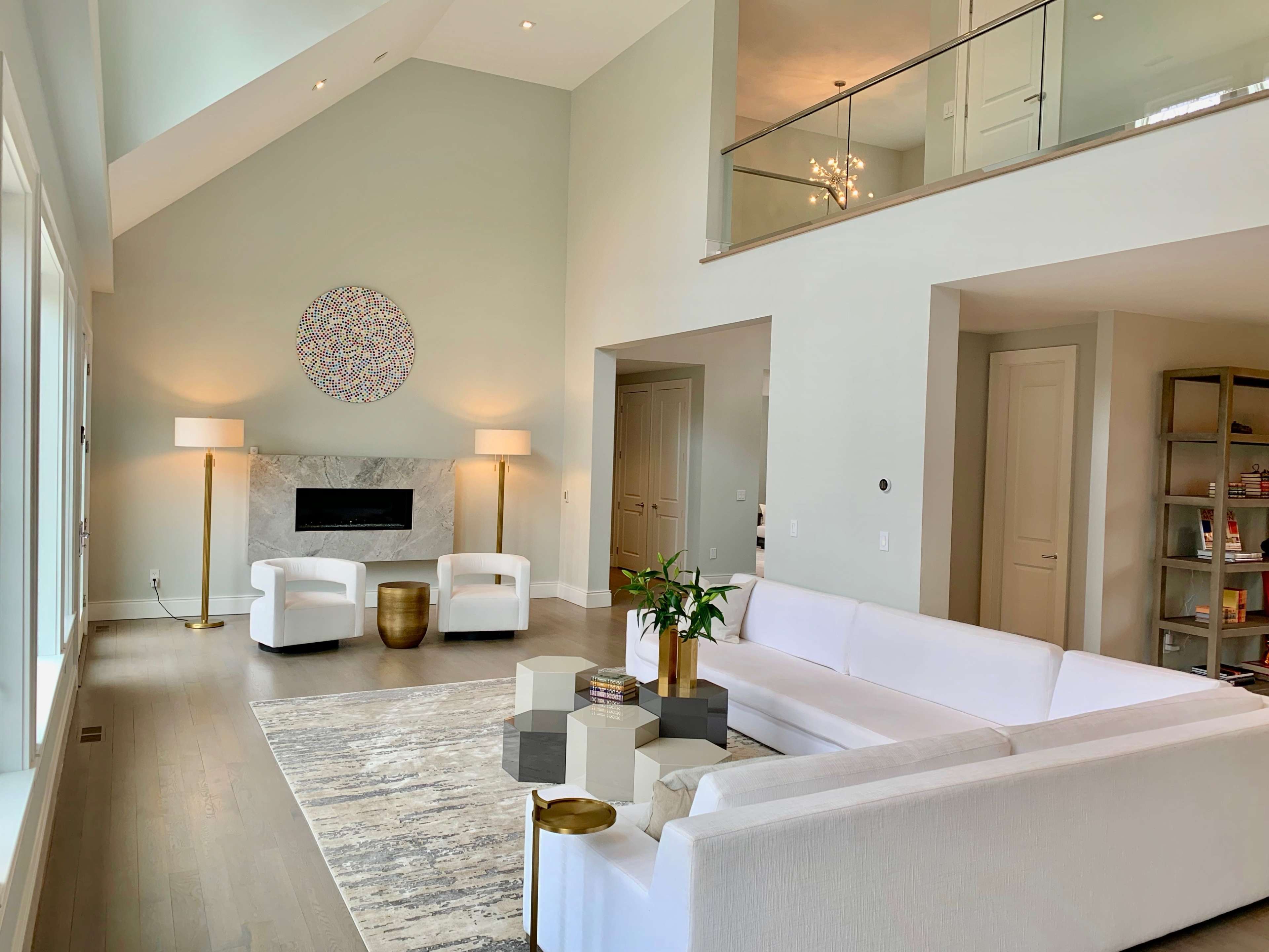 A modern living room with high ceilings, featuring a white sofa, two armchairs, a coffee table, and a decorative wall piece above a fireplace.