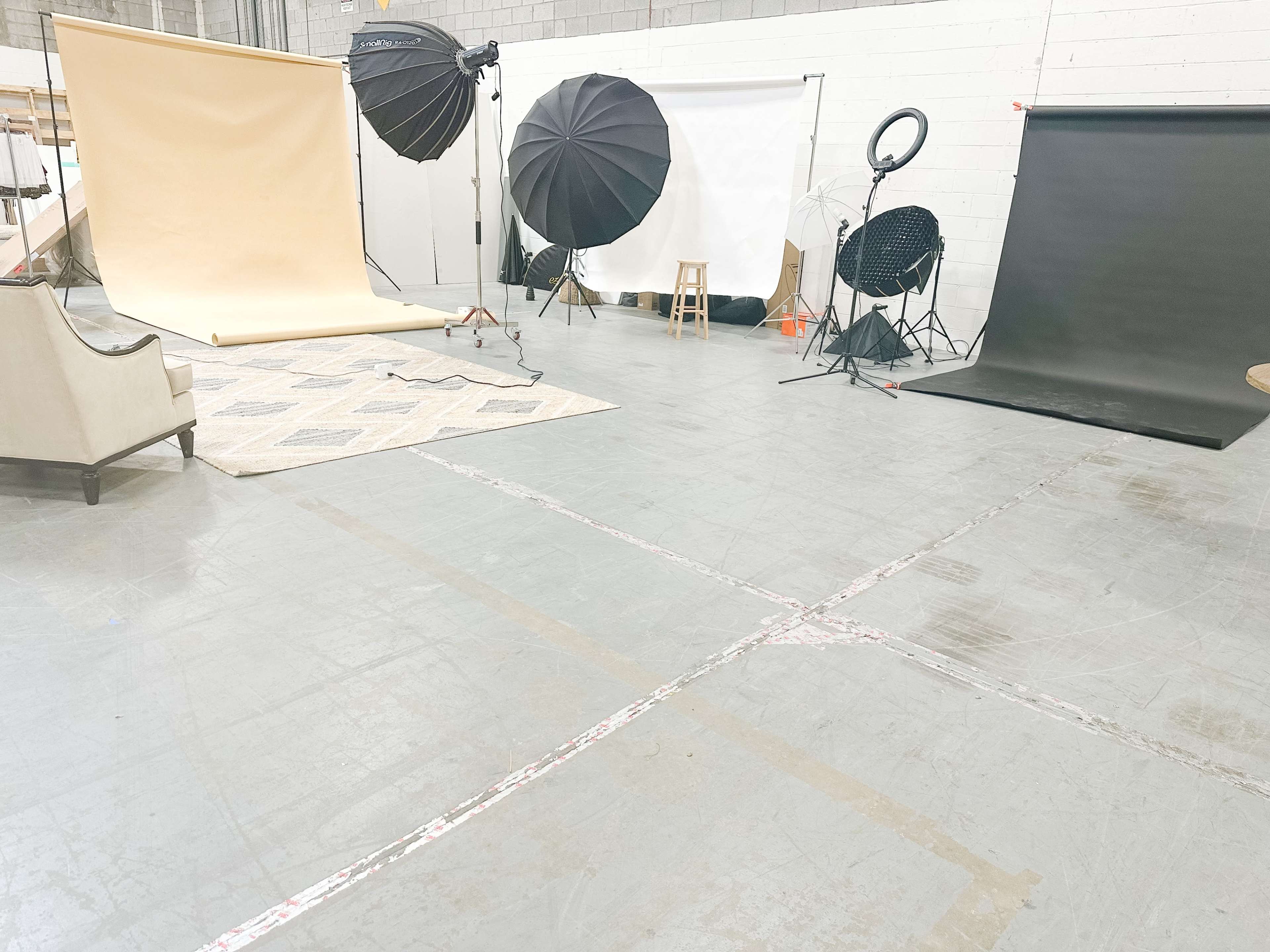 A photography studio setup with various backdrops, lighting equipment, and a chair on a patterned rug.